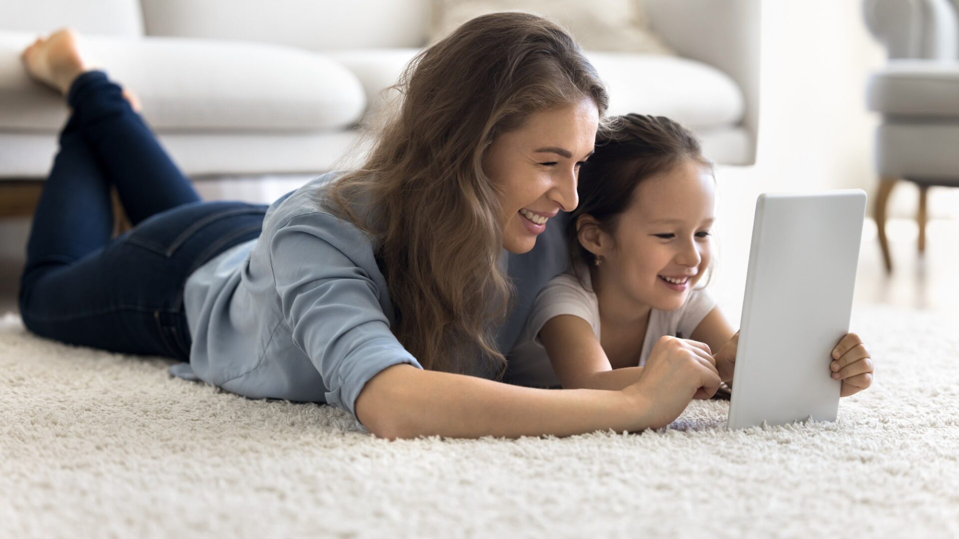 Mother and Daughter laying on carpet flooring play with ipad