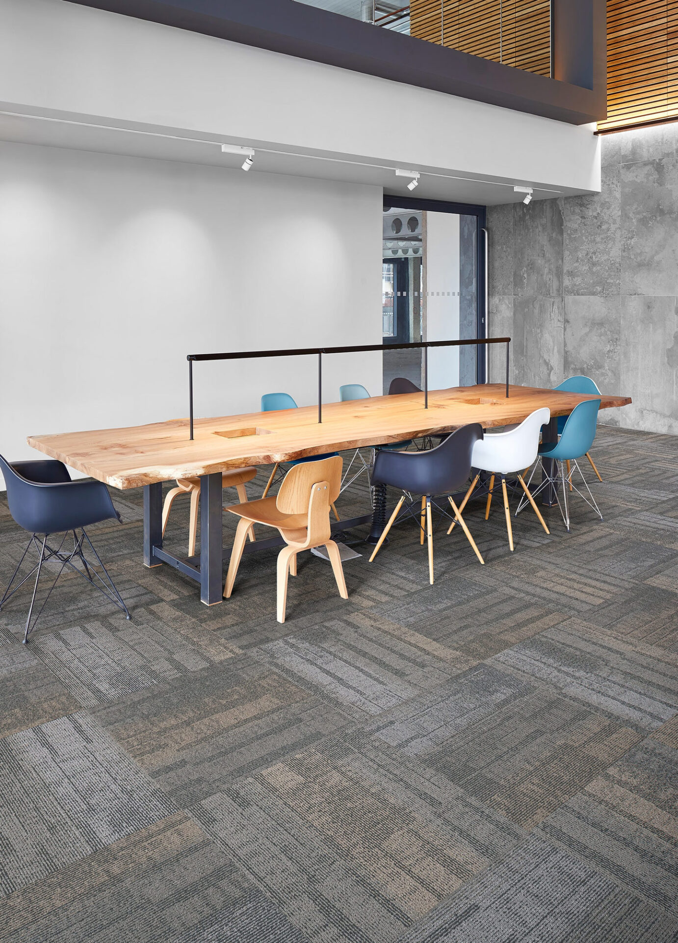Blue-gray carpet tile under a live-edge conference table with colorful molded chairs