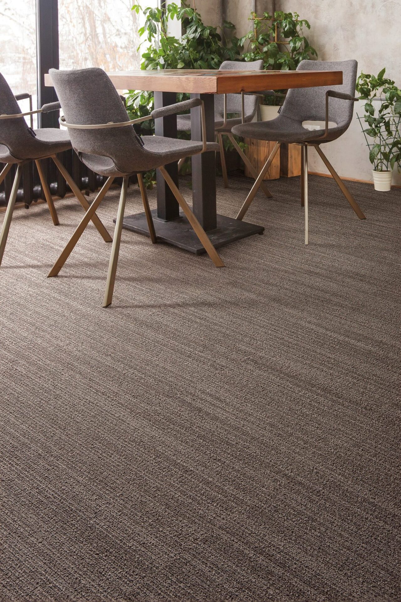 Break room or dining area with brown striated carpet, a wood table, gray upholstered chairs and potted plants