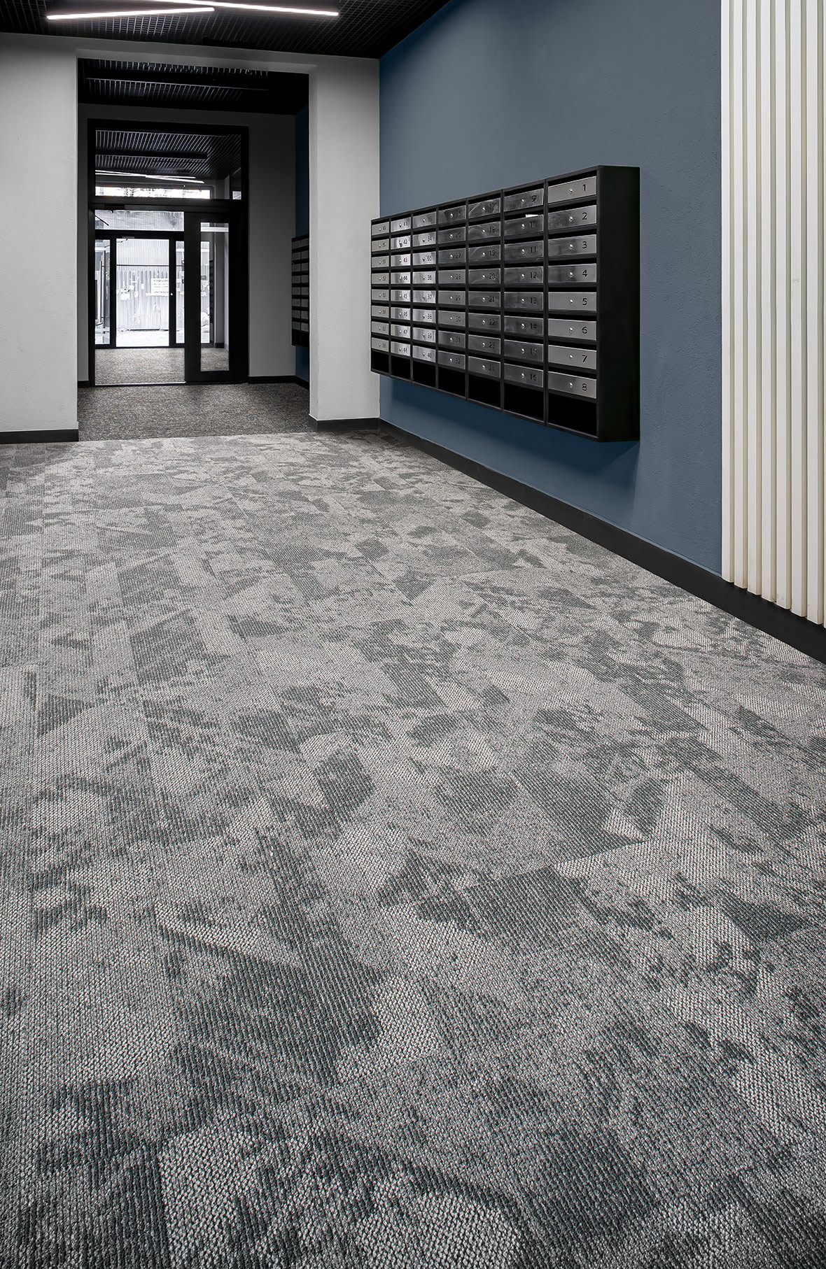 Building corridor with gray abstract patterned carpet tile, a blue accent wall and wall-mounted mailboxes