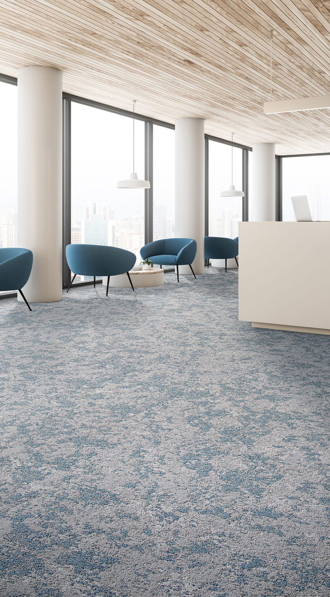 Bright lobby with blue and cream patterned carpet, blue lounge chairs, white columns and a wood slat ceiling
