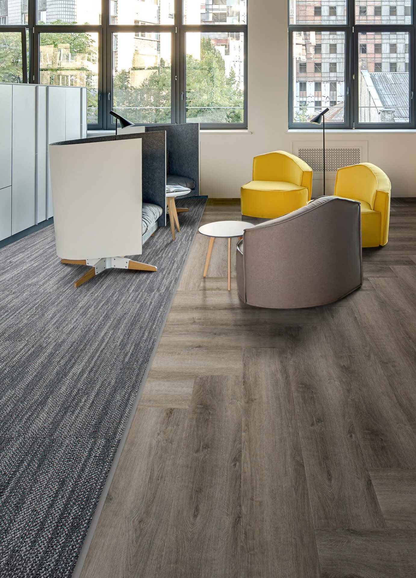 Open office with gray striped carpet tile beside wood-look vinyl plank, yellow lounge chairs and tall windows