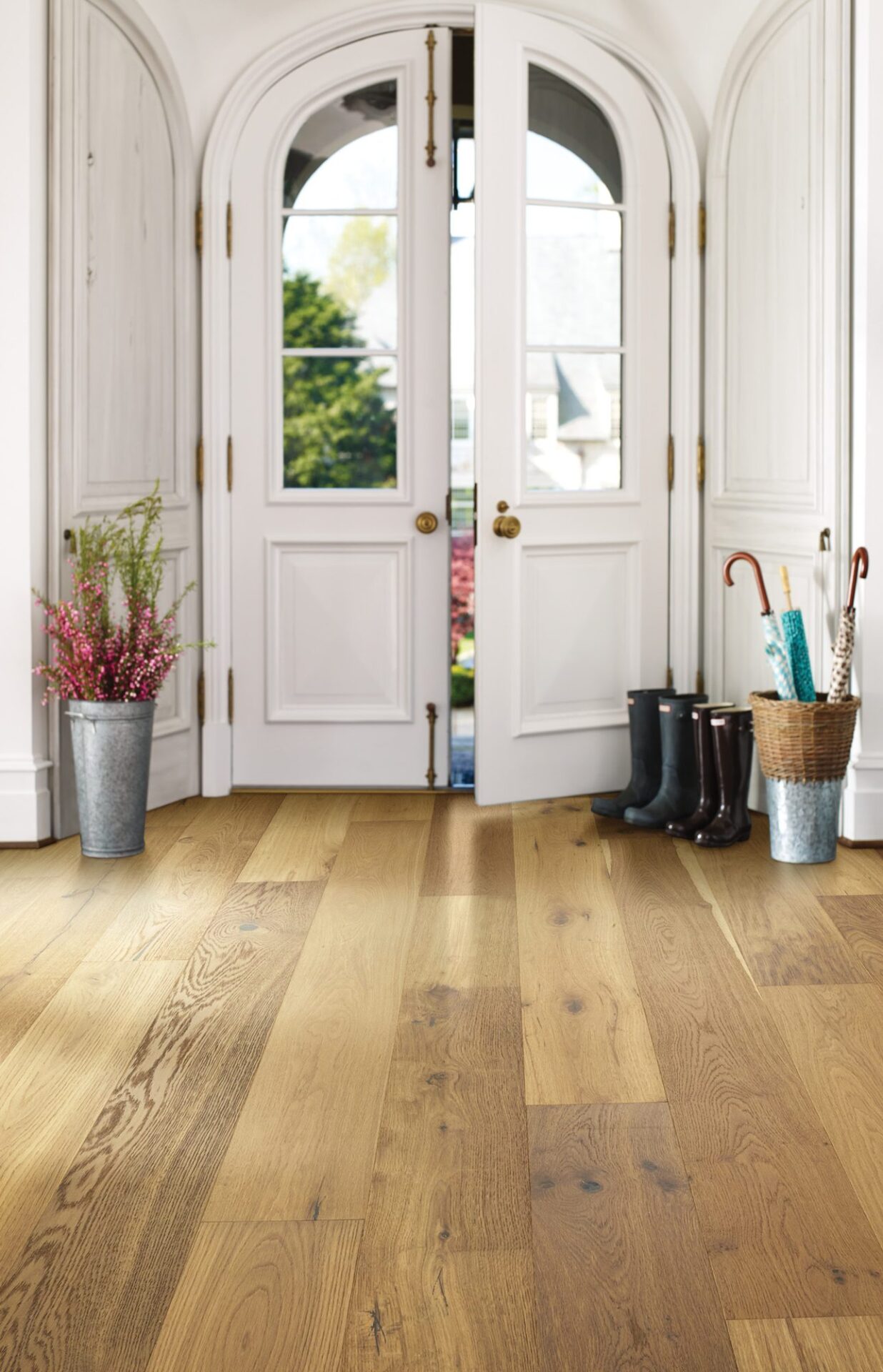 Wide light oak hardwood planks in a bright entry with white arched double doors, rain boots and potted flowers