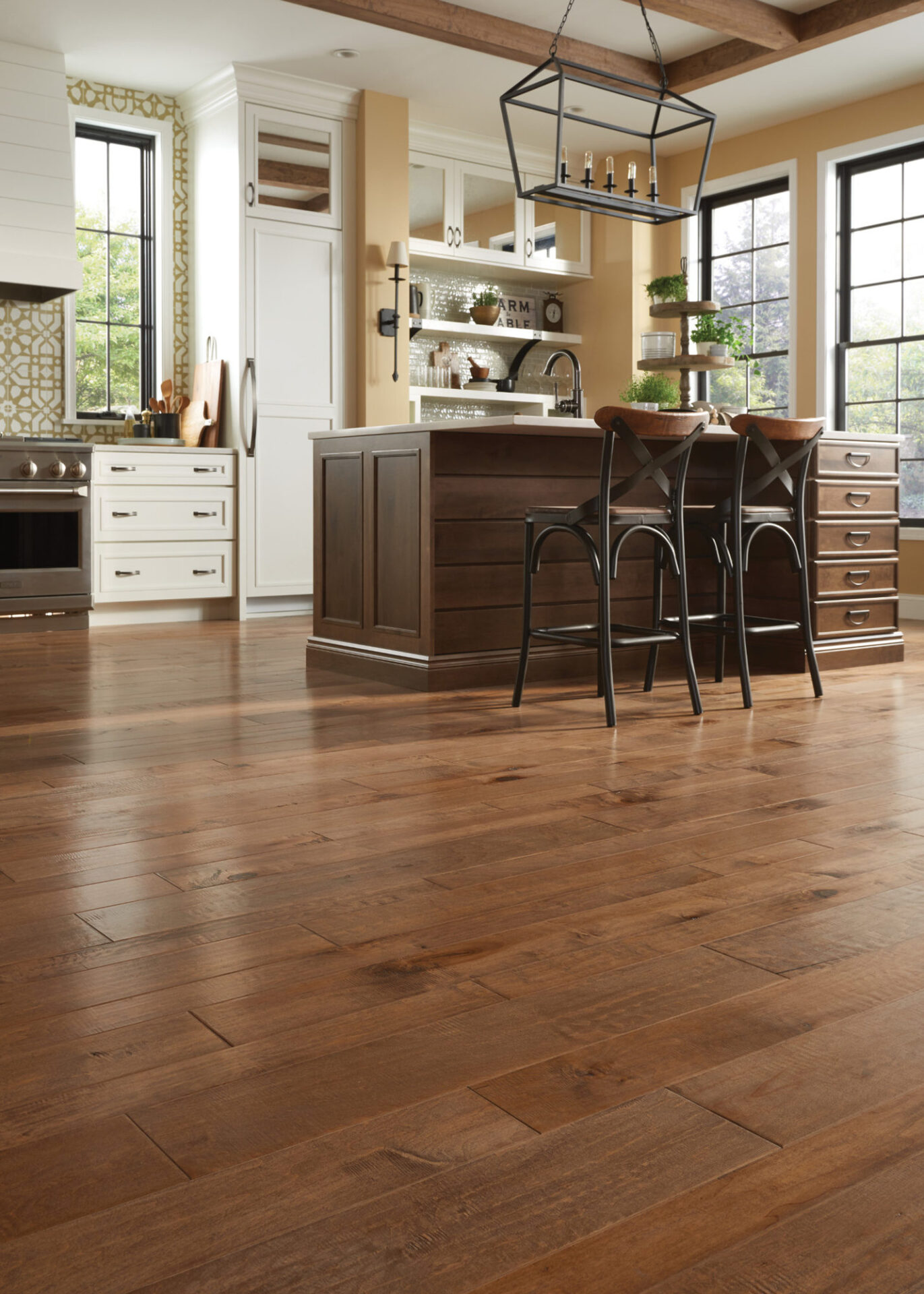 Warm mixed-width maple hardwood flooring in a farmhouse kitchen with a dark island and stools