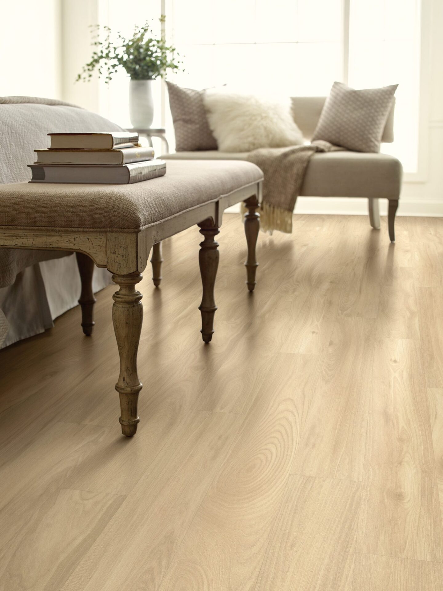 Bright bedroom with light oak-look laminate, a carved wood bench at the foot of the bed and a cream settee