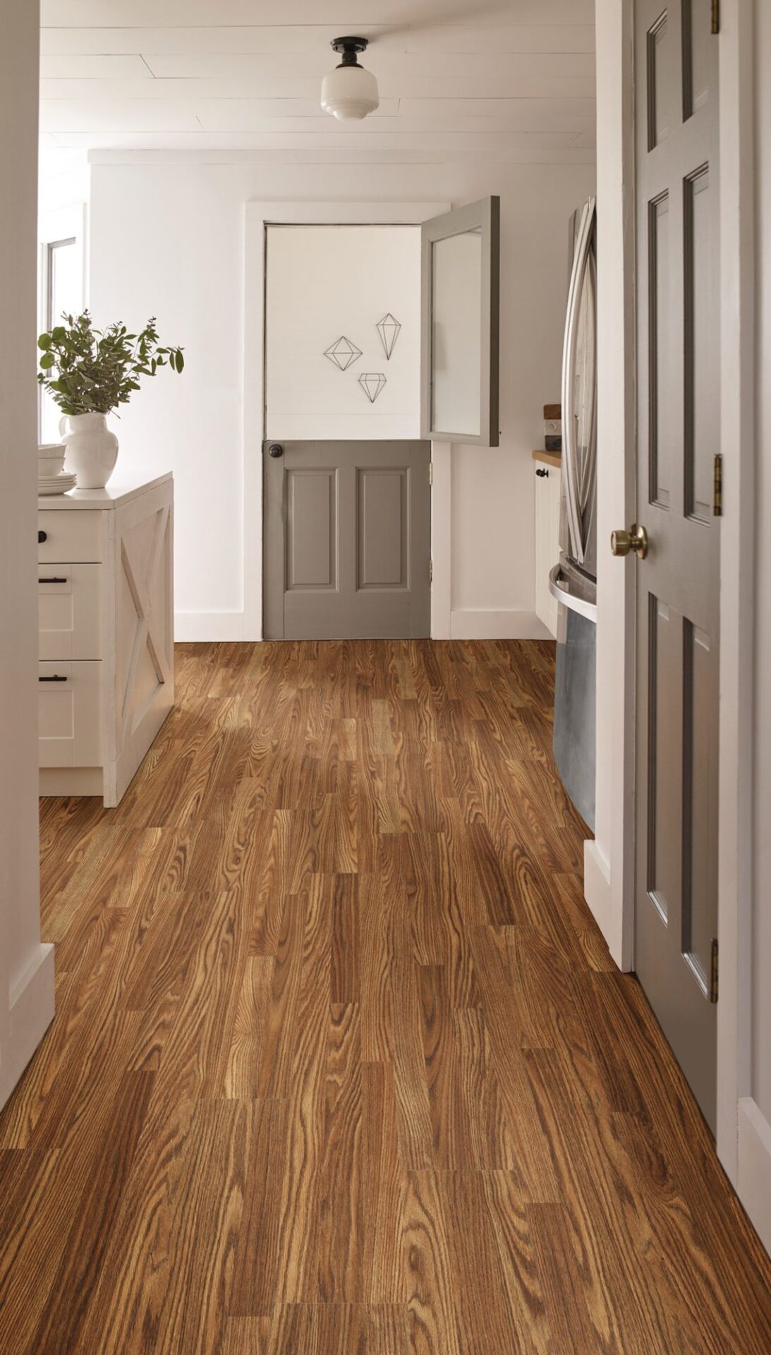 Hallway leading to a white kitchen with warm reddish wood-look laminate planks and a gray dutch door at the end