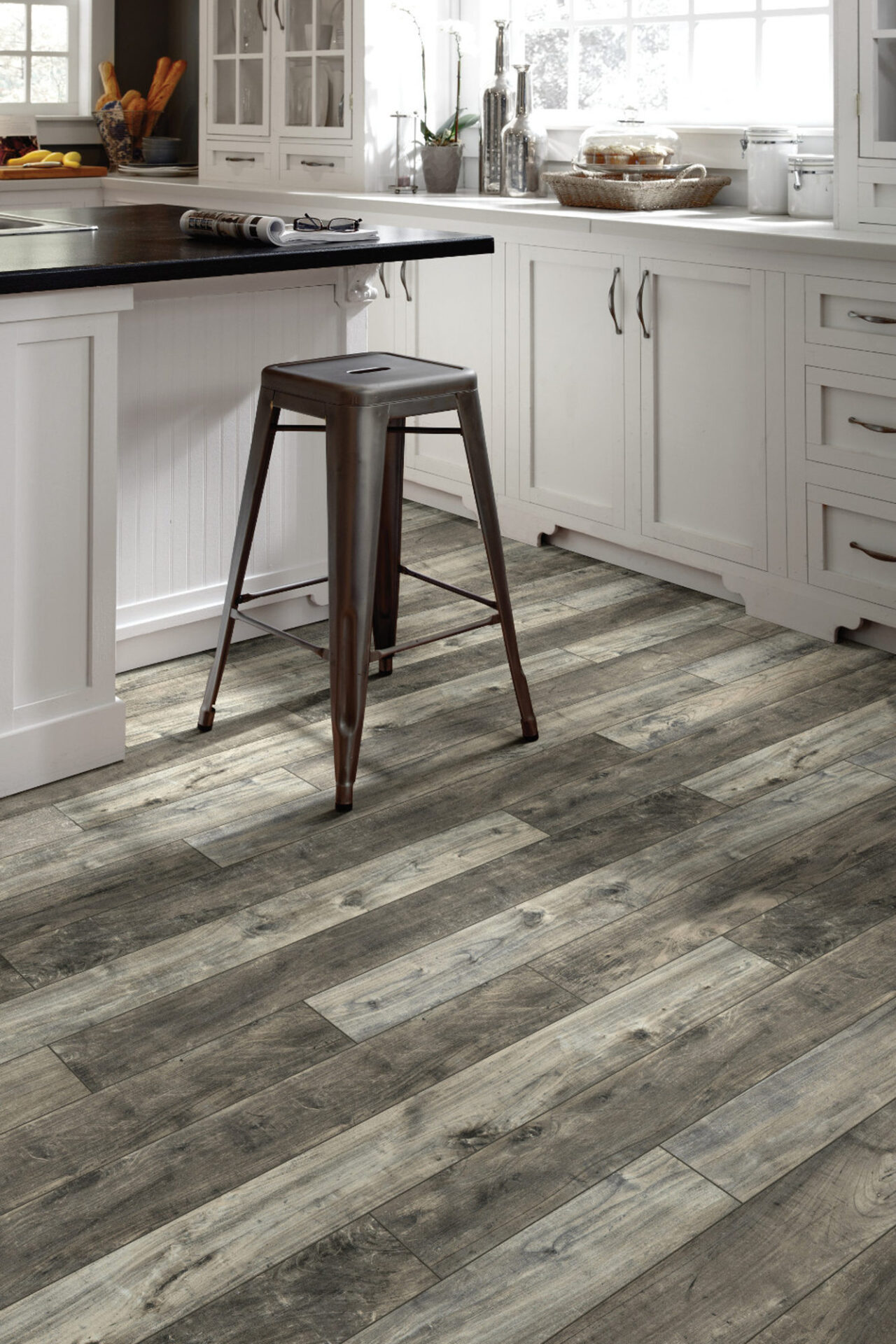 Rustic gray wood-look laminate plank flooring in a white kitchen with a metal counter stool