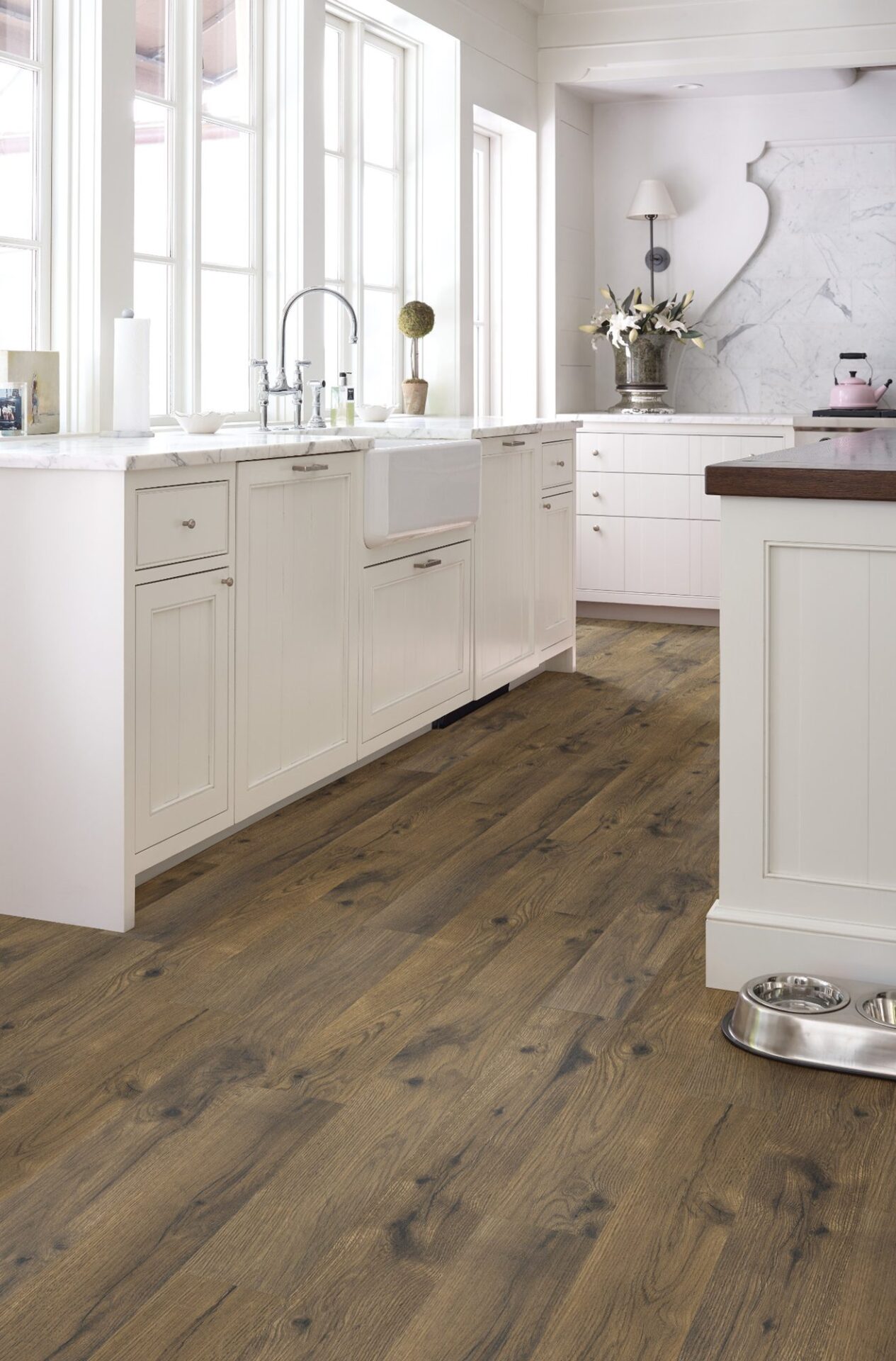 White farmhouse kitchen with rustic brown oak-look laminate floor, a farmhouse sink and a pet bowl by the island
