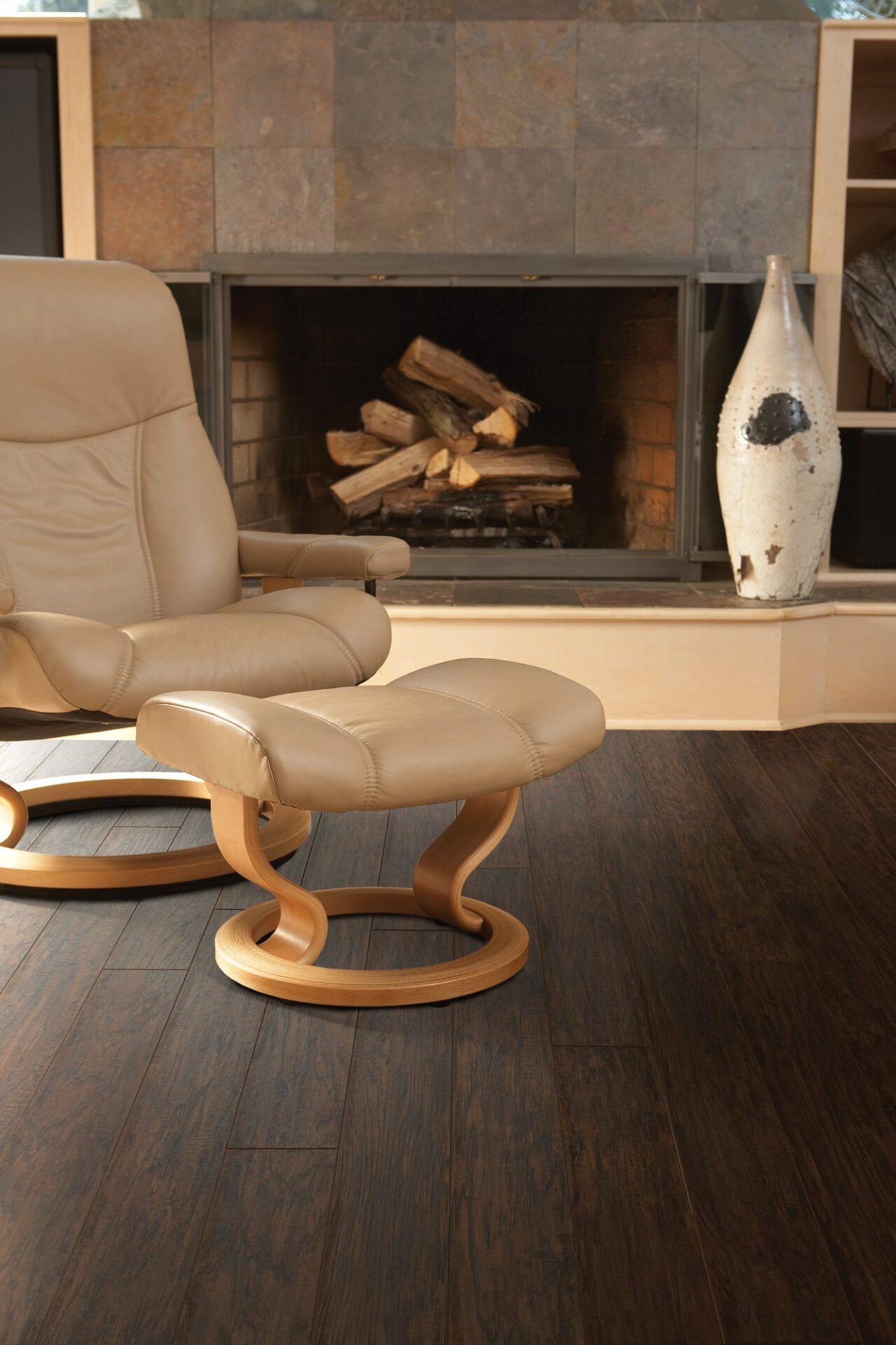 Family room with dark hickory-look laminate, a tan leather recliner and ottoman in front of a wood-burning fireplace