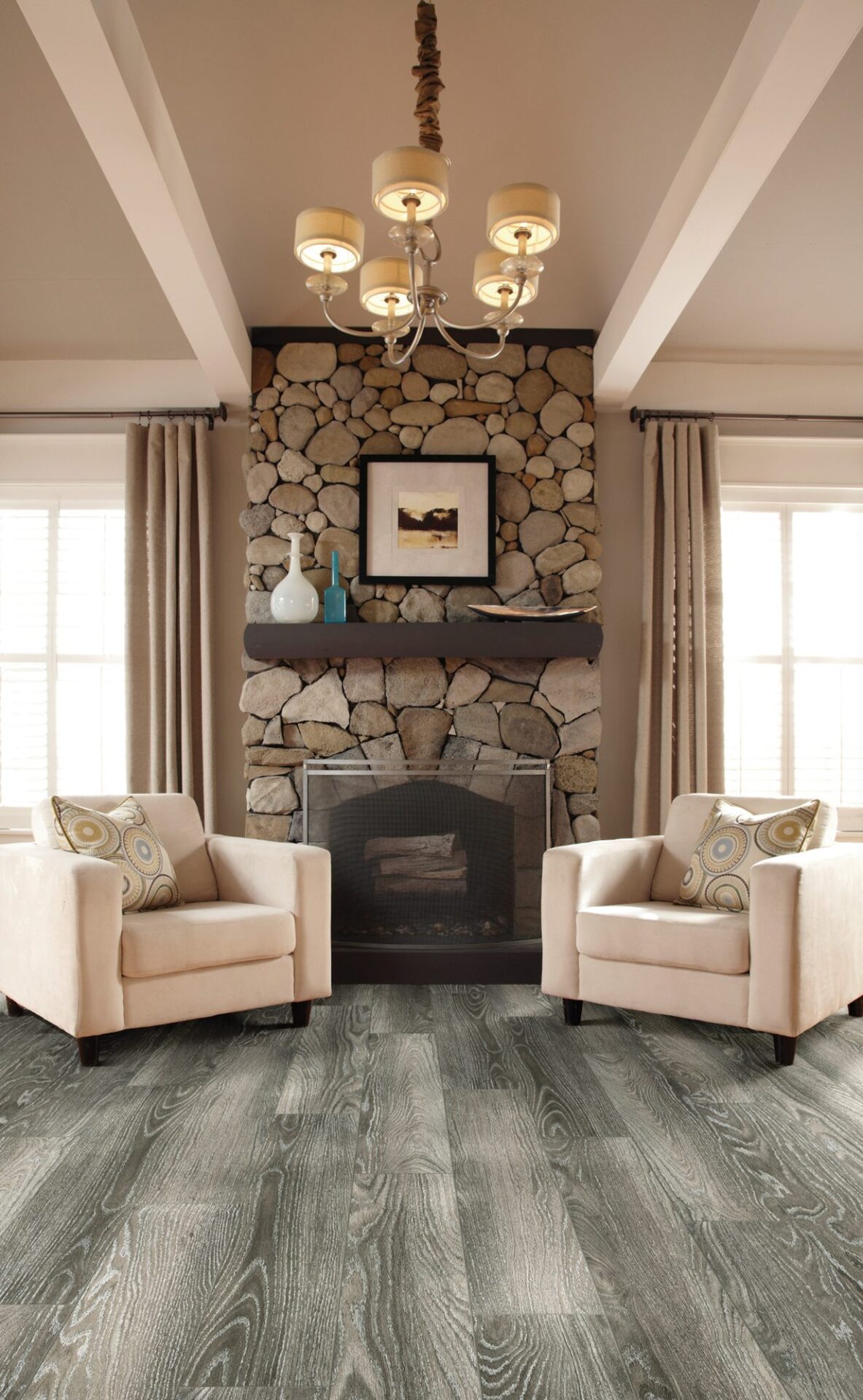 Family room with gray oak-look laminate, two cream armchairs facing a stone fireplace under a chandelier