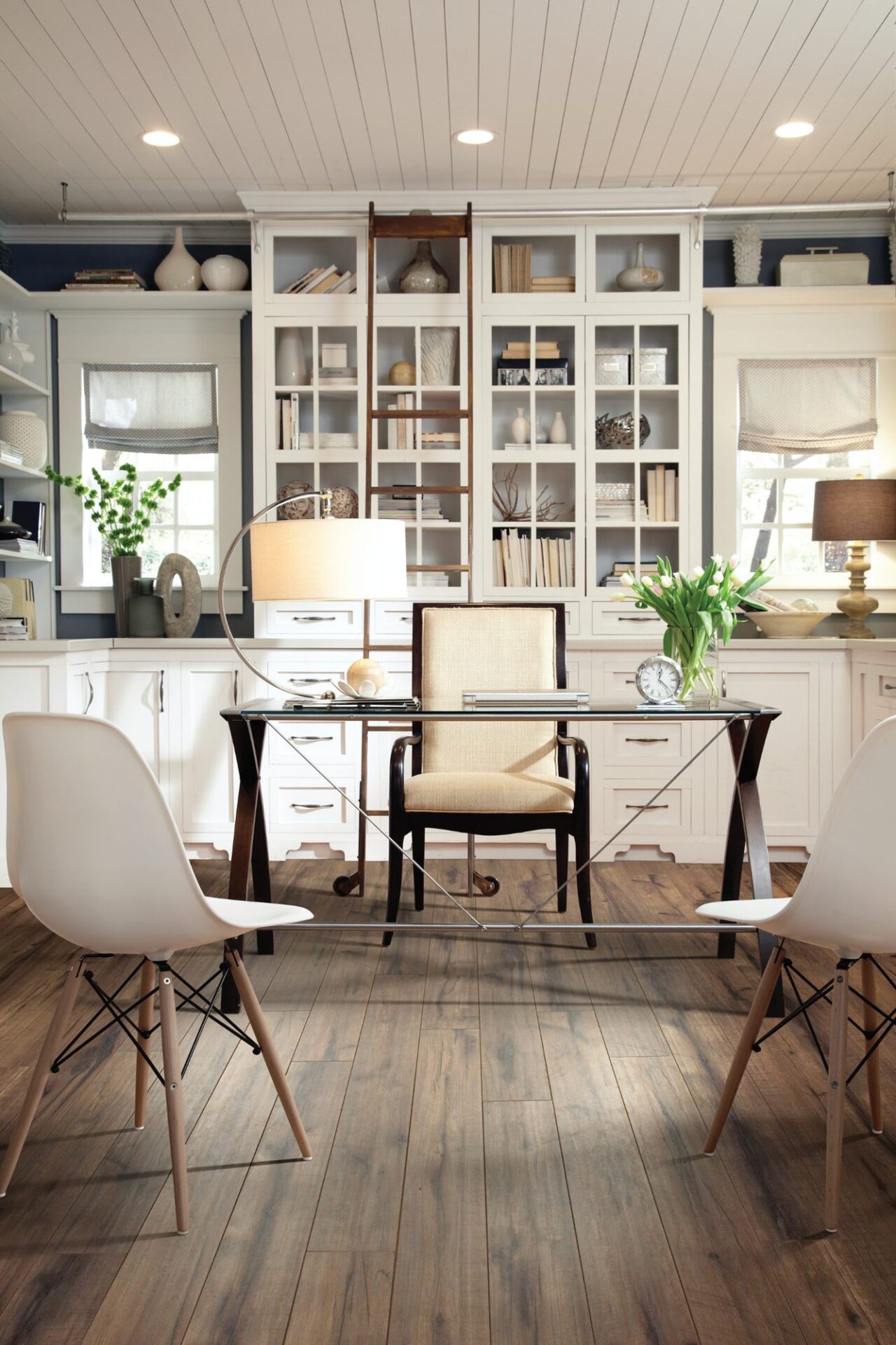 Home office with rustic hickory-look laminate, a glass desk, white chairs and white built-in bookshelves