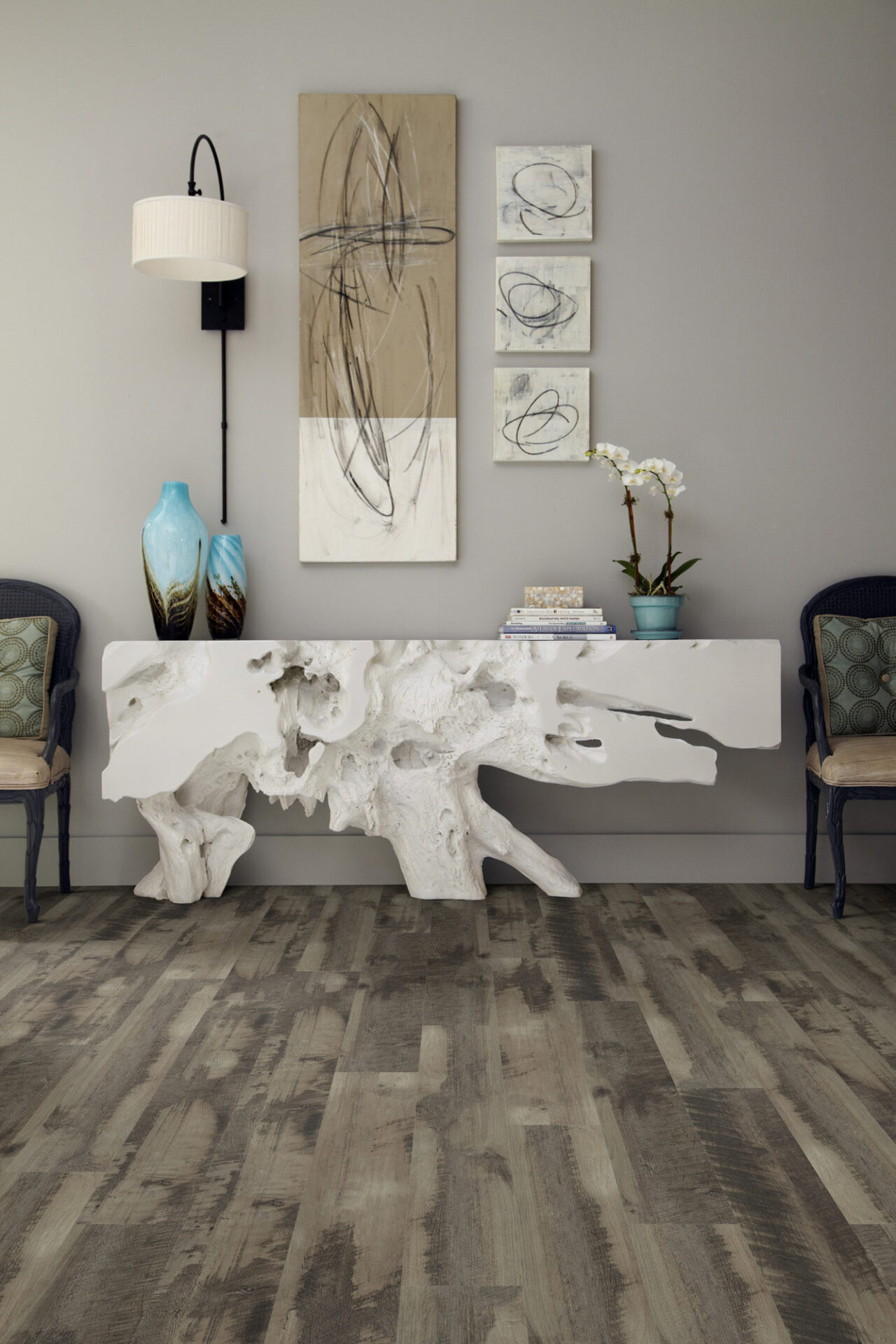 Weathered gray-brown wood-look vinyl plank in an entry with a sculptural console table