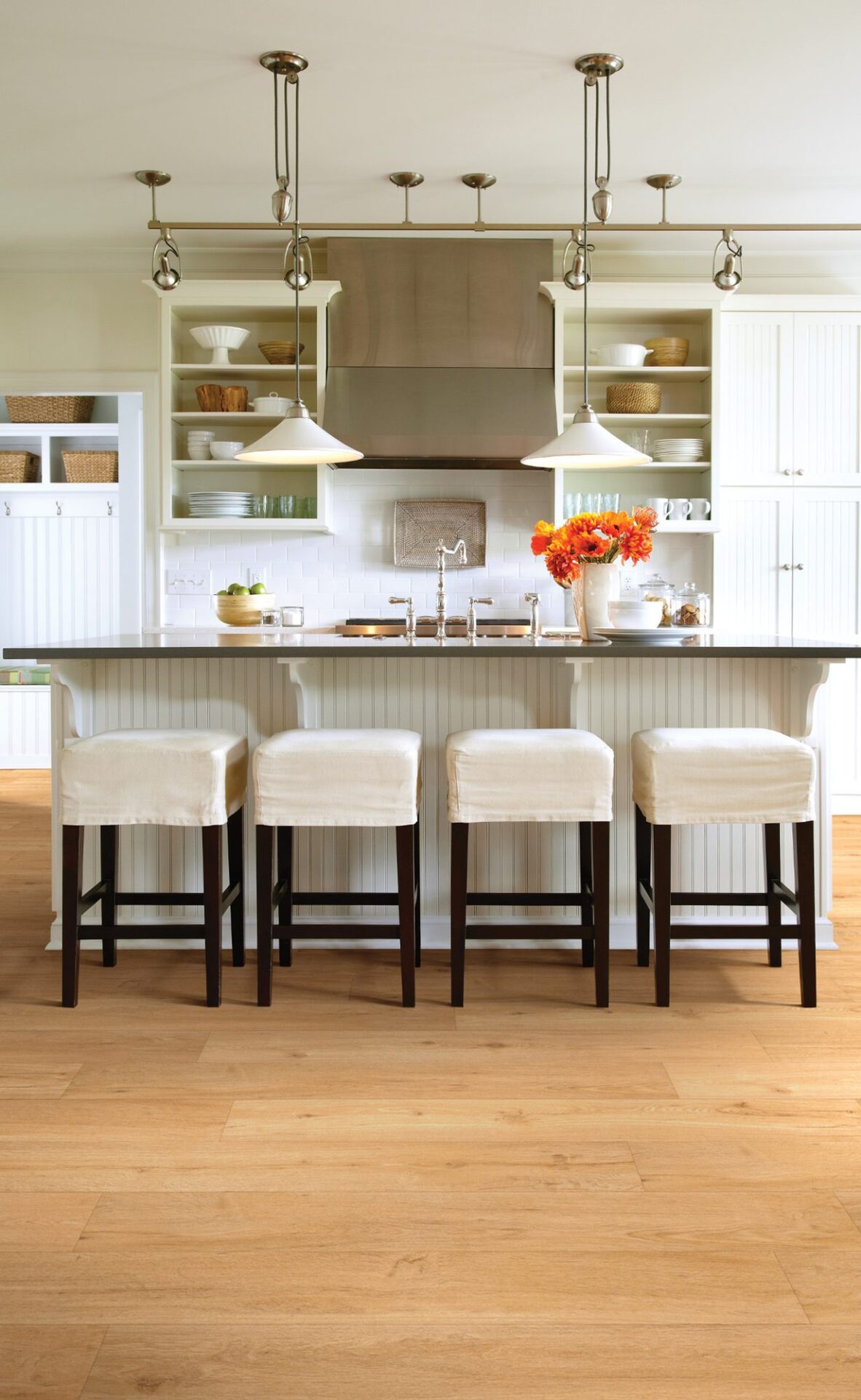 Honey oak look vinyl plank floor in a white kitchen with an island and four slipcovered stools