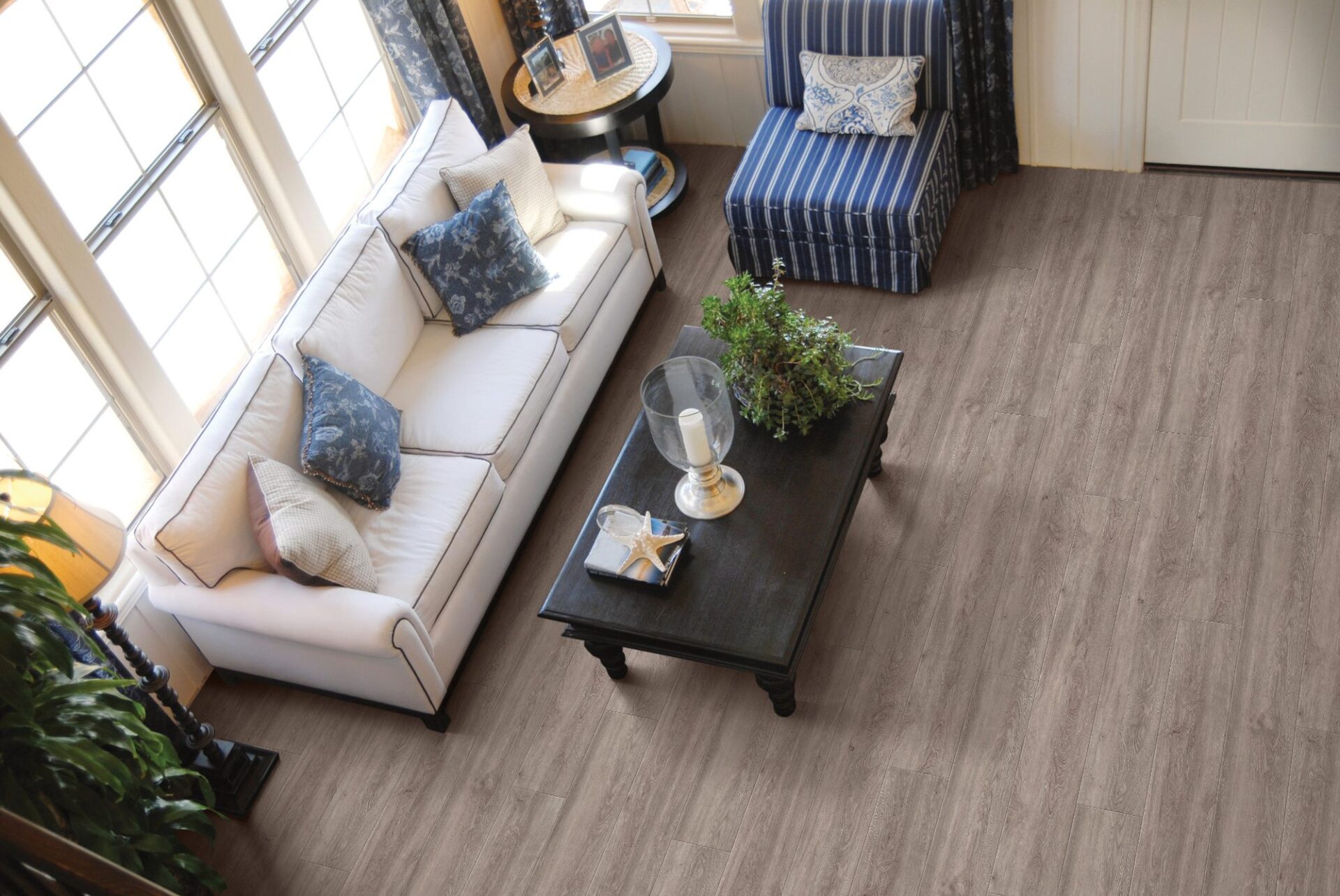 Overhead view of a living room with grayed oak look vinyl plank, white sofa, blue armchairs and dark coffee table