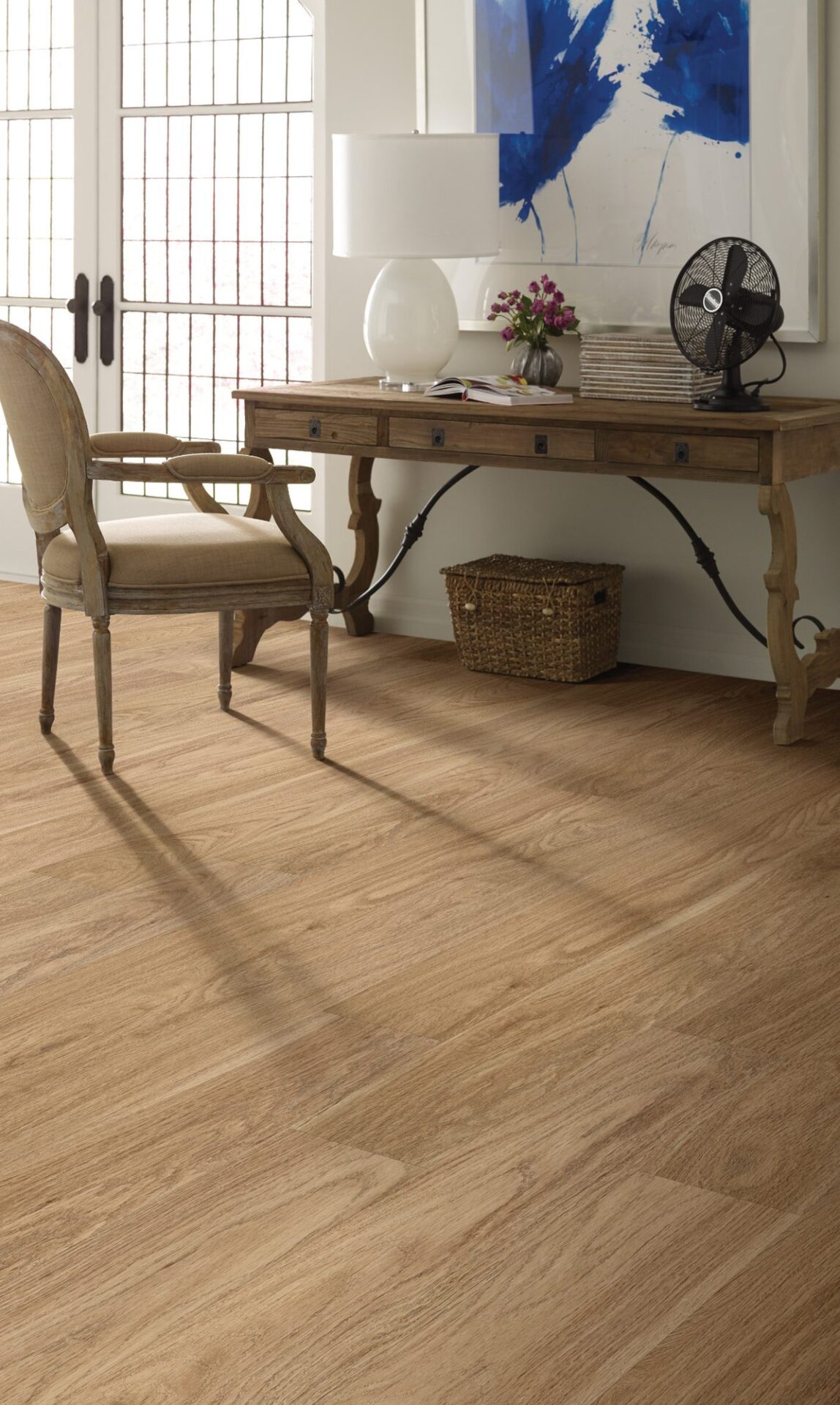 Natural oak look vinyl plank in a home office with a carved wood desk, desk lamp and fan