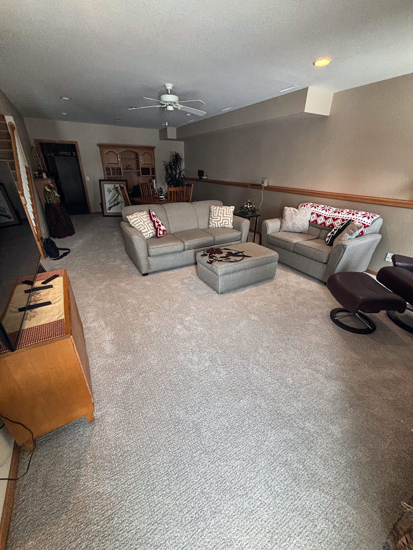 Light neutral carpet across a long basement family room with sofas and a ceiling fan