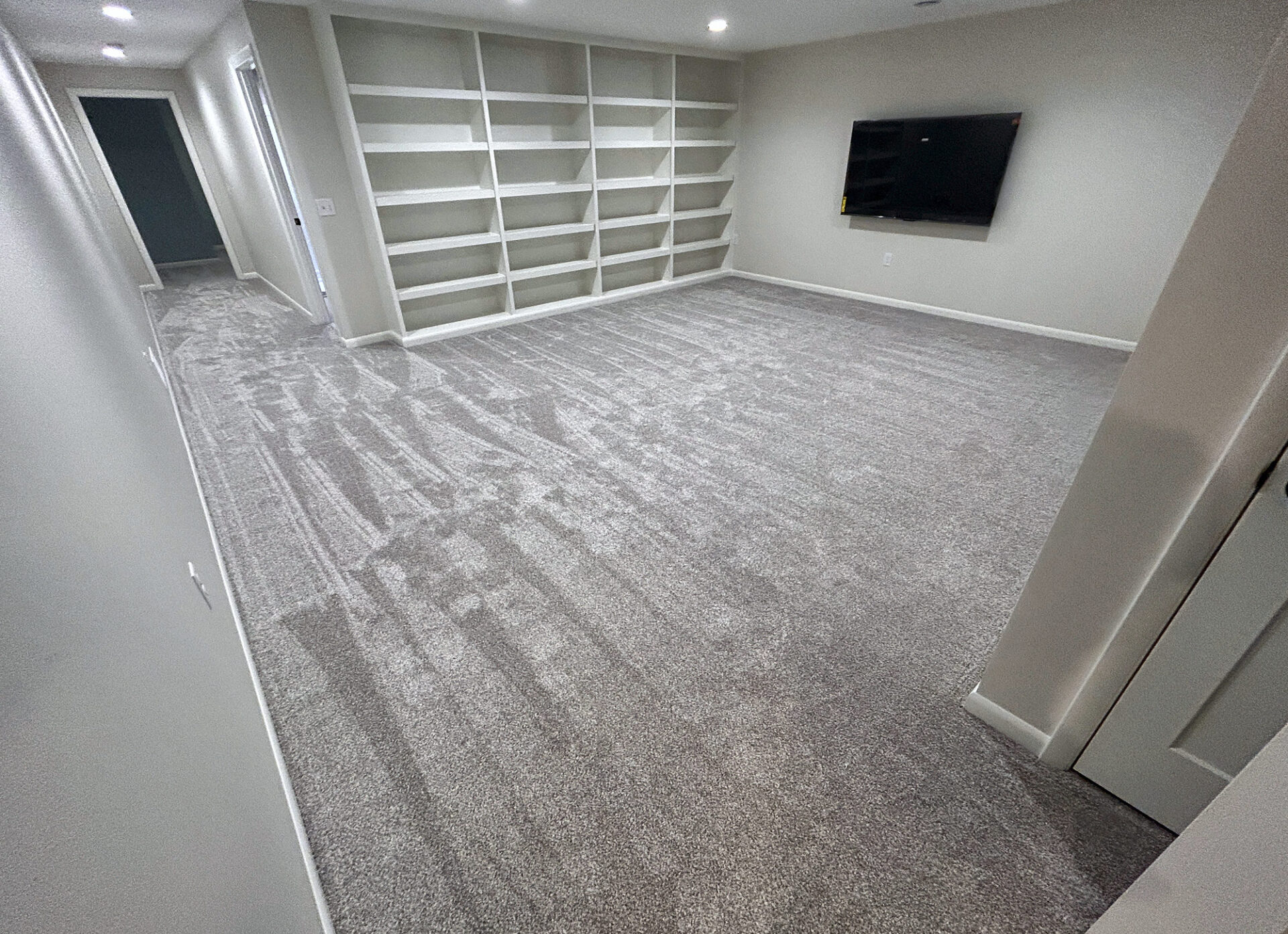 Soft light gray carpet in a basement media room with built-in shelves and a wall TV