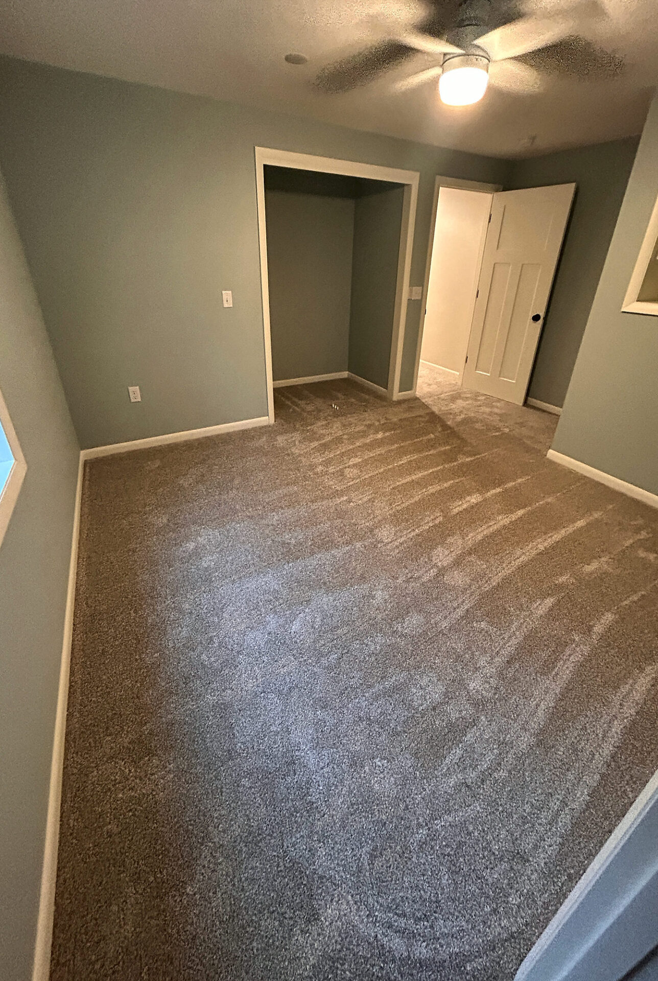Soft light gray carpet in an empty bedroom with an open closet and ceiling fan