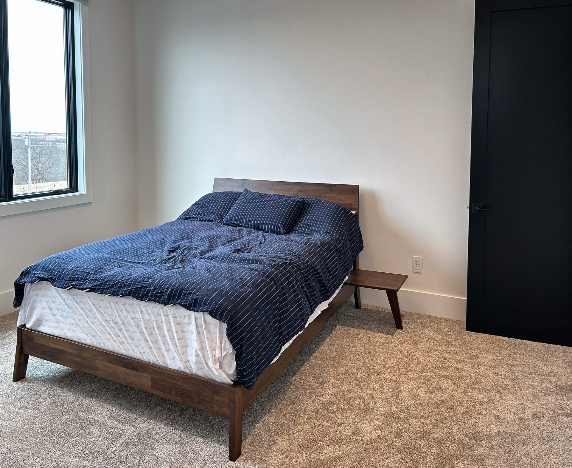 Plush beige carpet in a bright guest bedroom with a wood bed frame and black door