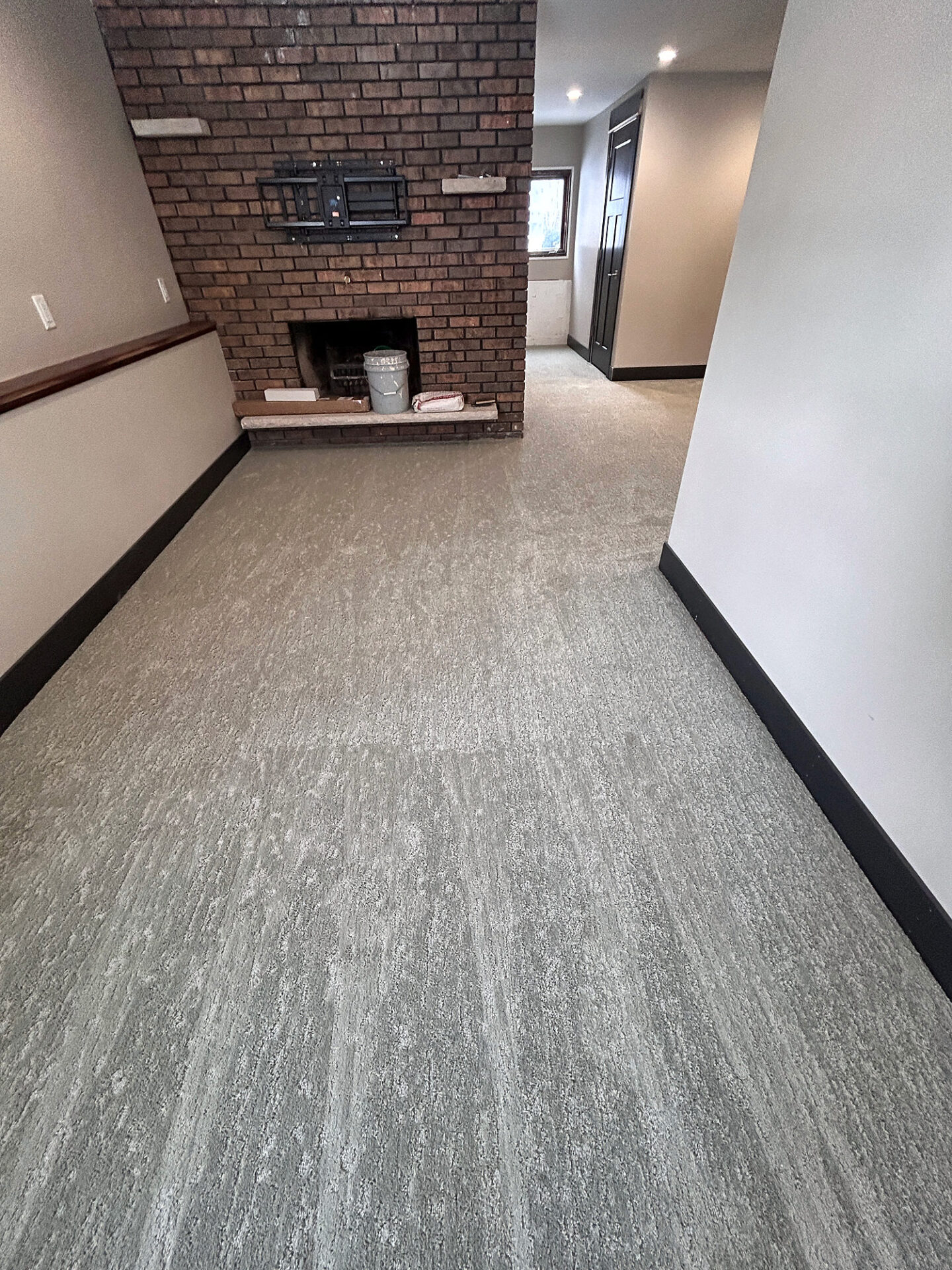 Gray patterned carpet in a long living room with a brick fireplace and black baseboards