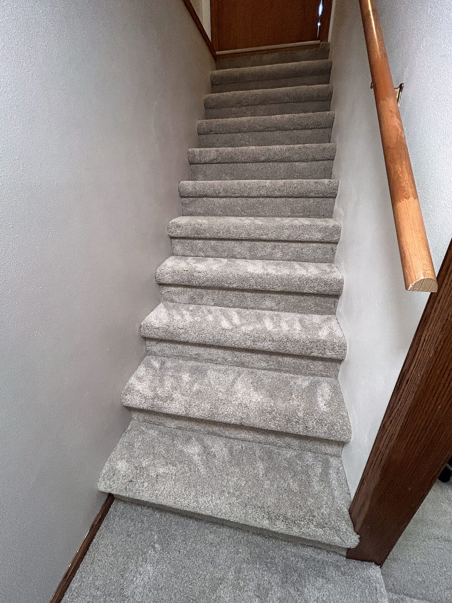 Plush light gray carpet installed on a long straight staircase with a wood handrail