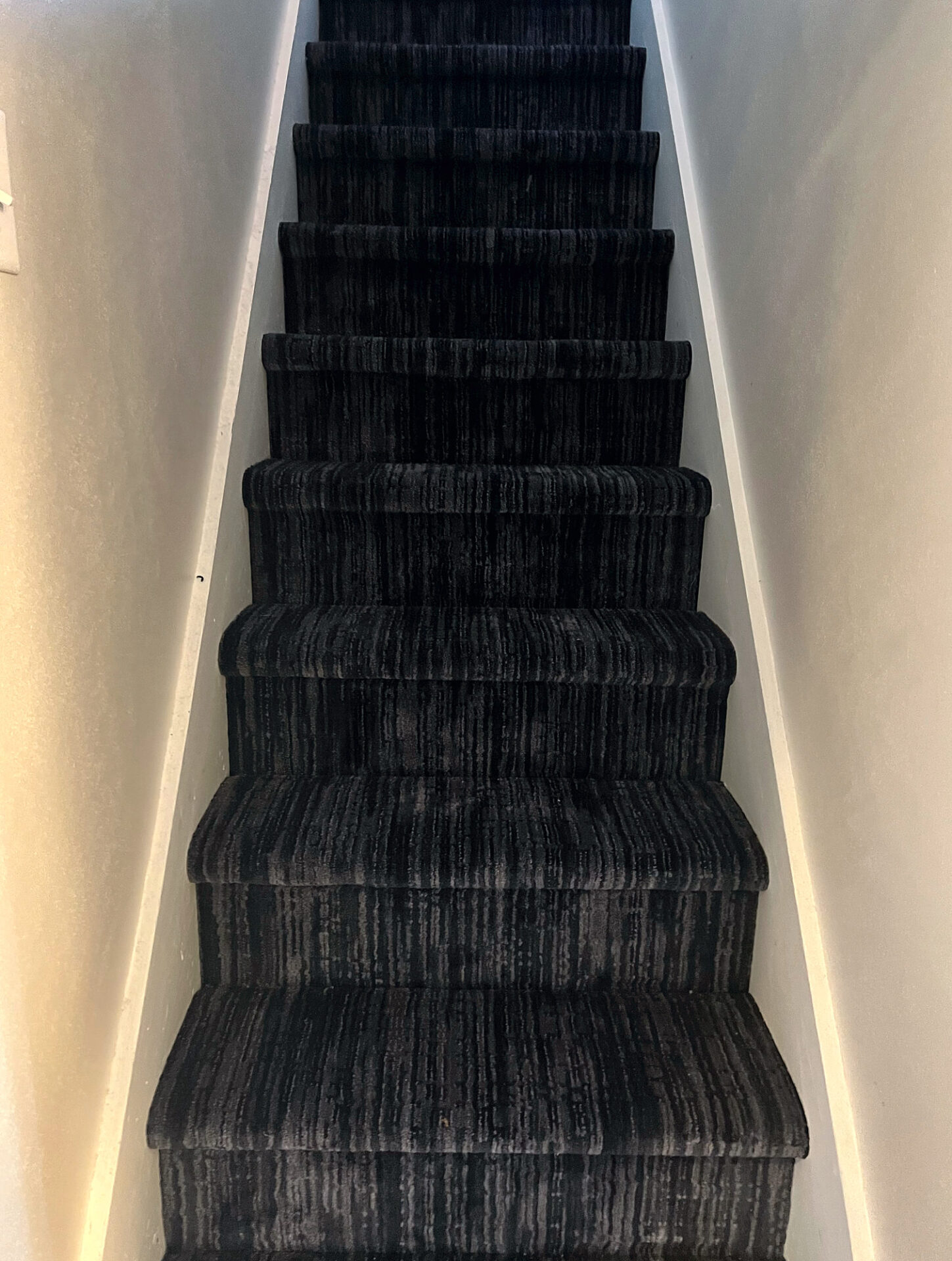 Dark striped carpet on a narrow staircase with soft wall lighting along the steps