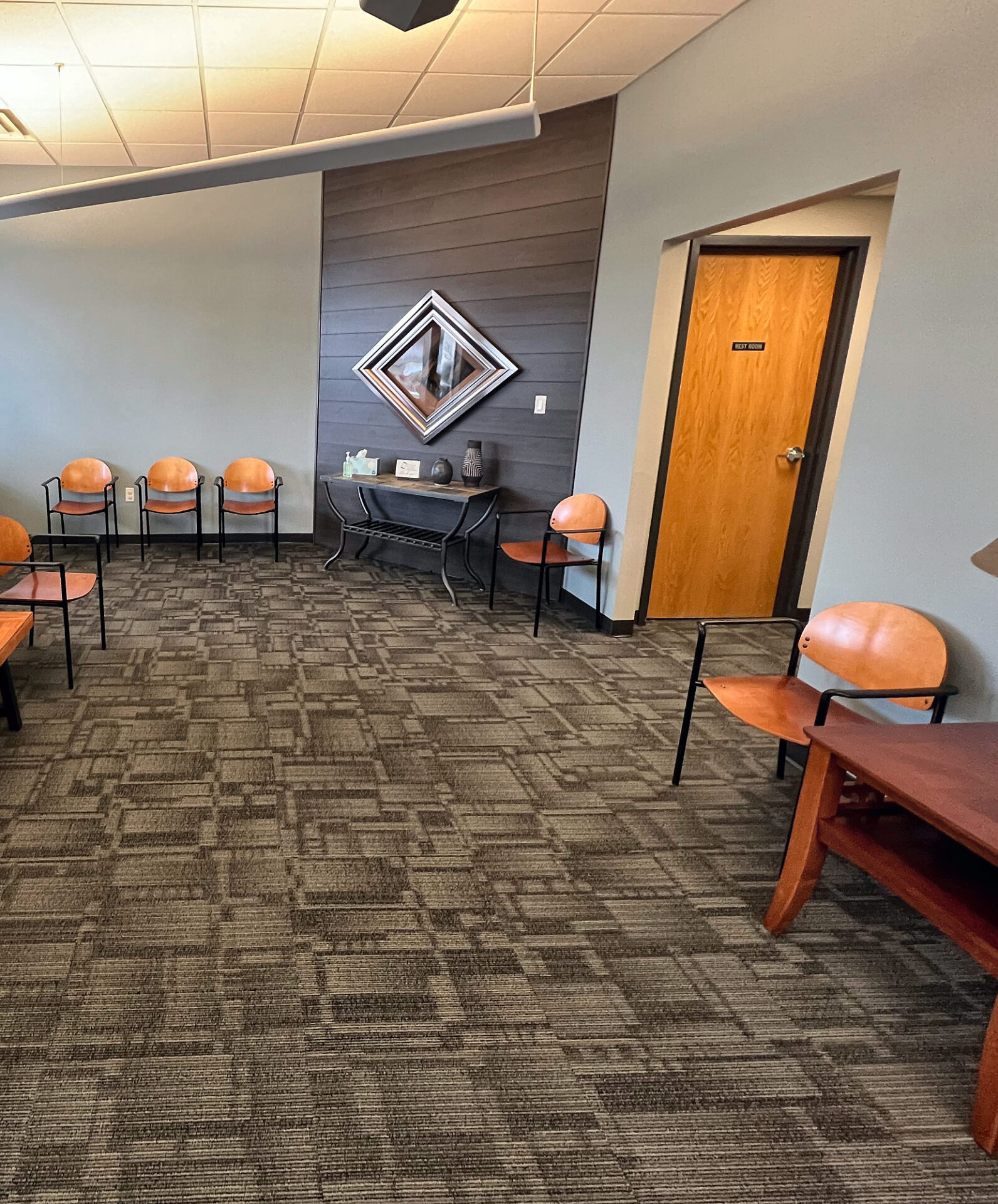 Brown commercial carpet tile in a clinic waiting room with orange chairs and a wood door
