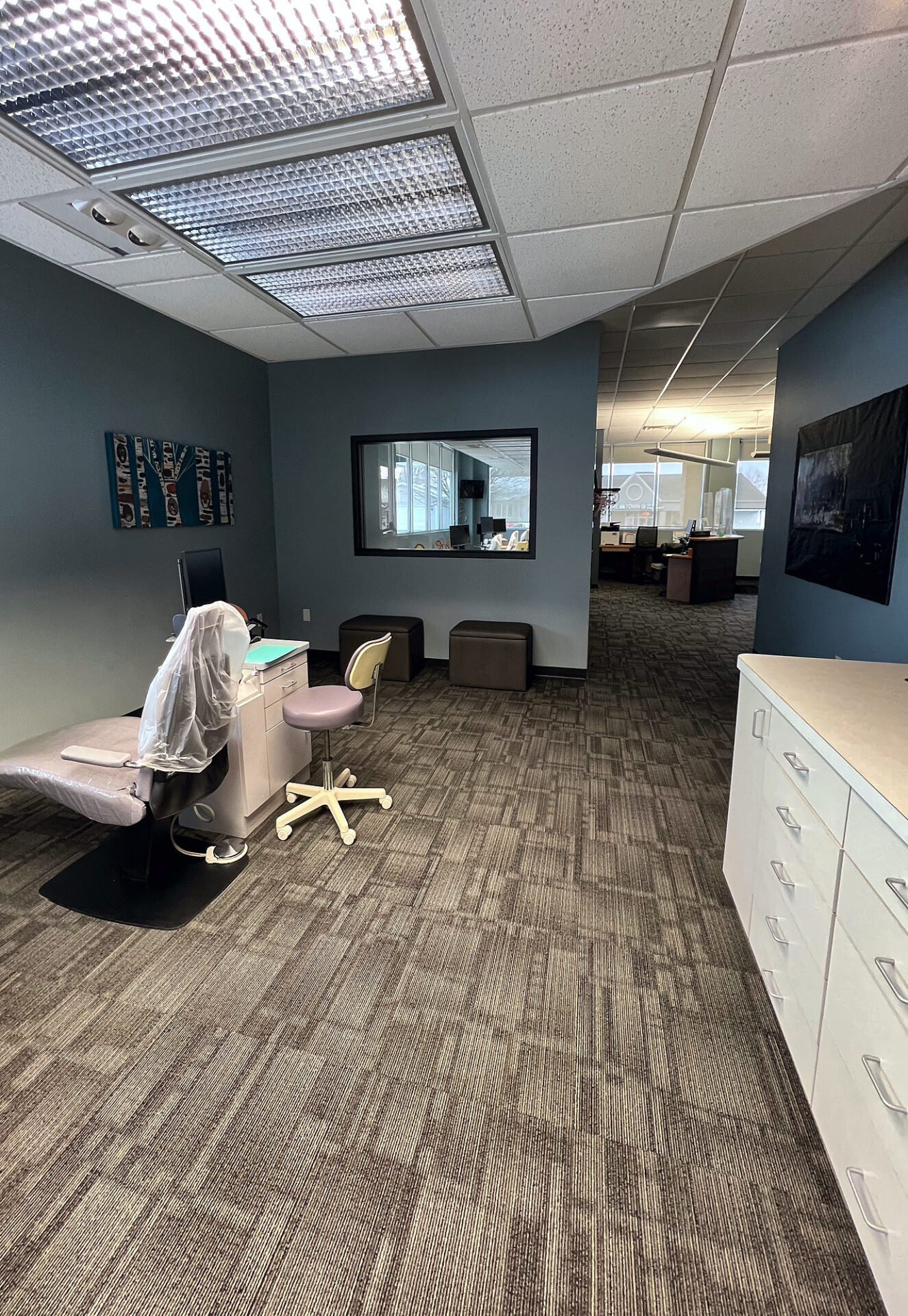Brown commercial carpet tile across an open clinic treatment area with cabinets and a chair