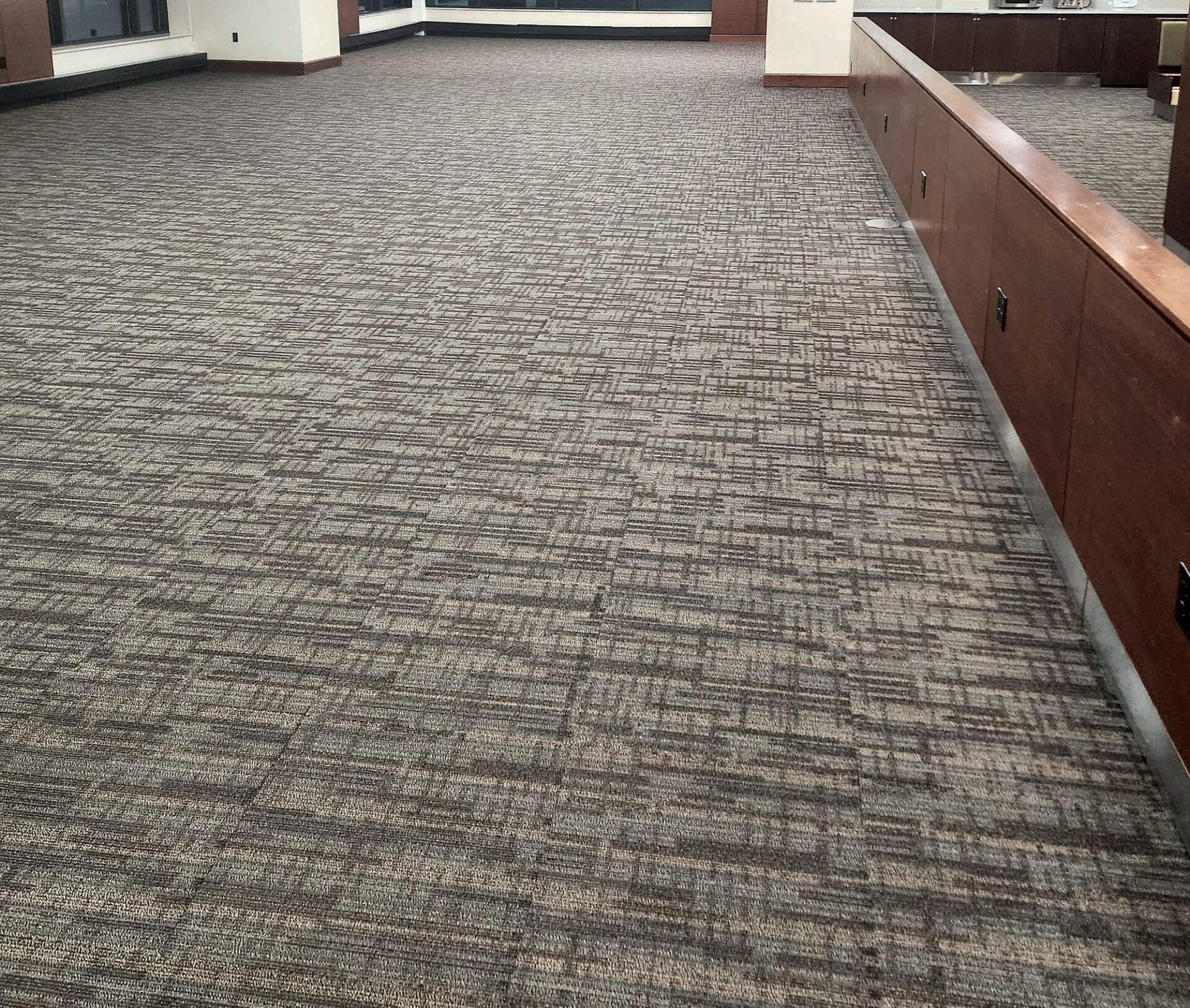 Brown and gray linear commercial carpet tile across an open lounge beside a wood half wall
