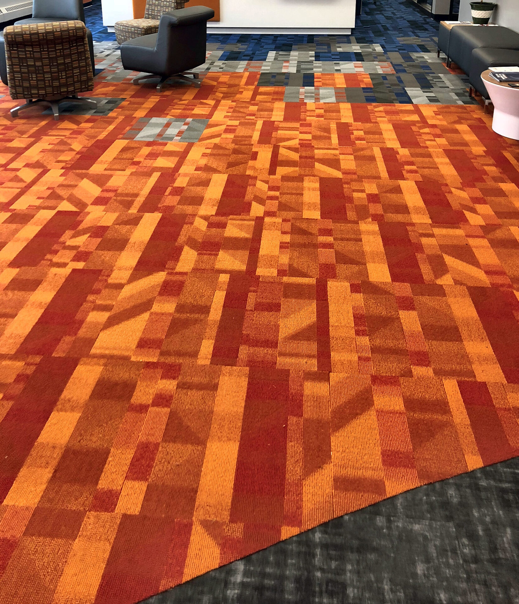 Bold orange and red patterned commercial carpet tile in a bright university lobby seating area