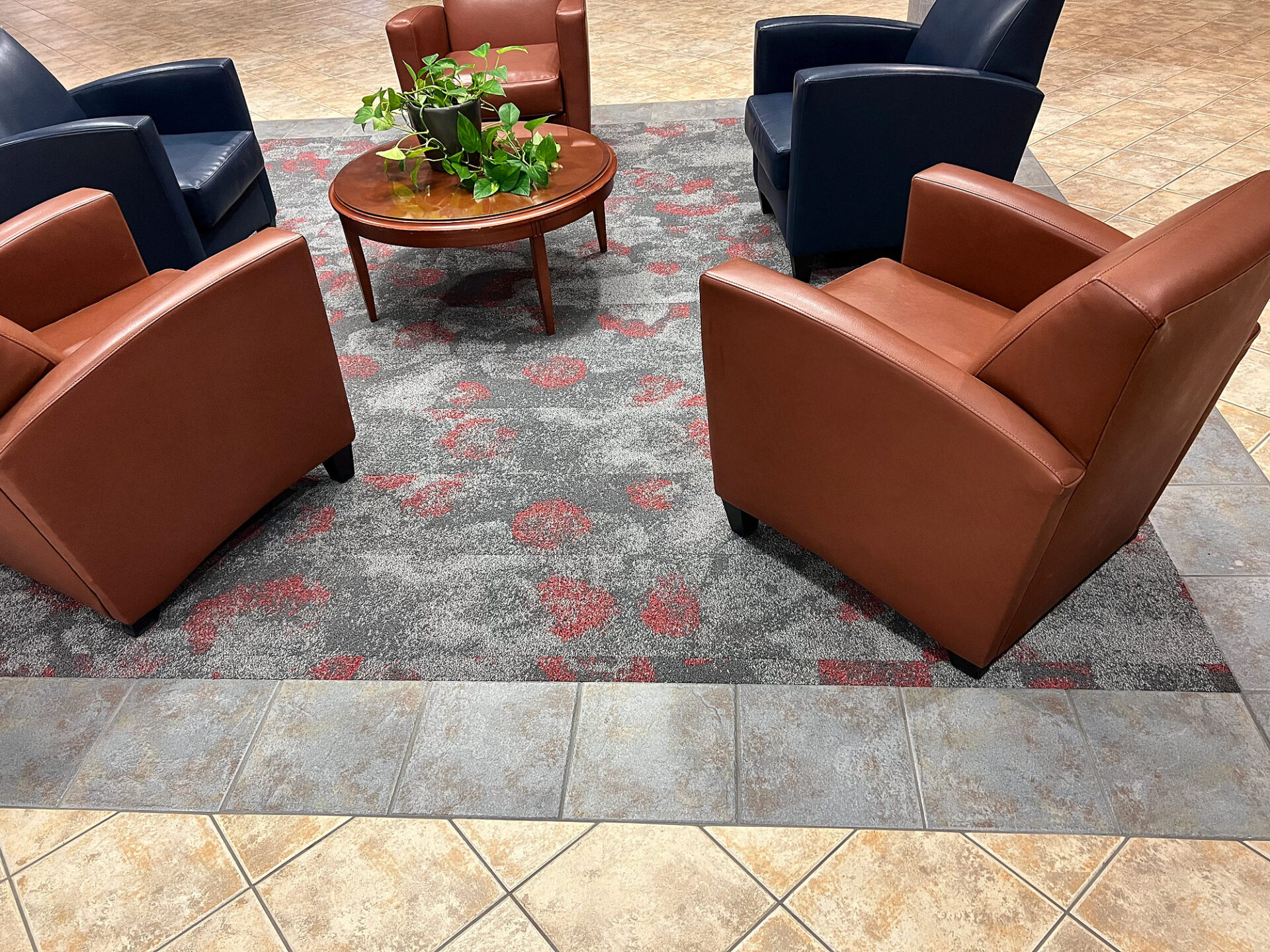 Gray and red patterned carpet inset framed by beige porcelain tile under lobby seating