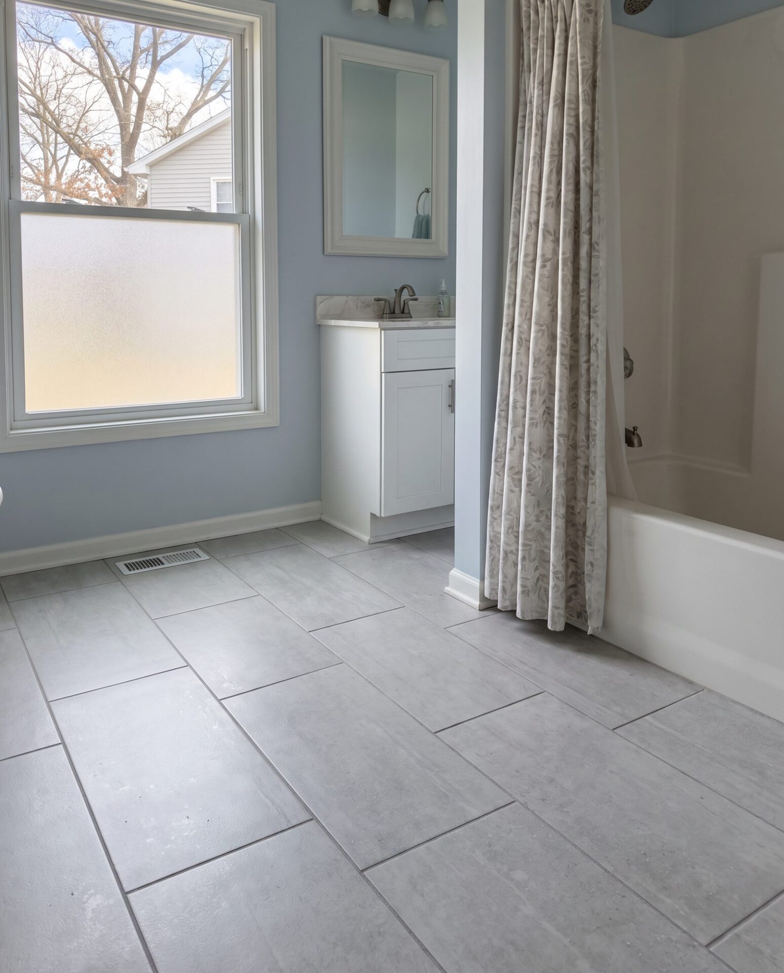 Light gray 12x24 porcelain tile in an offset pattern in a hall bathroom with a tub