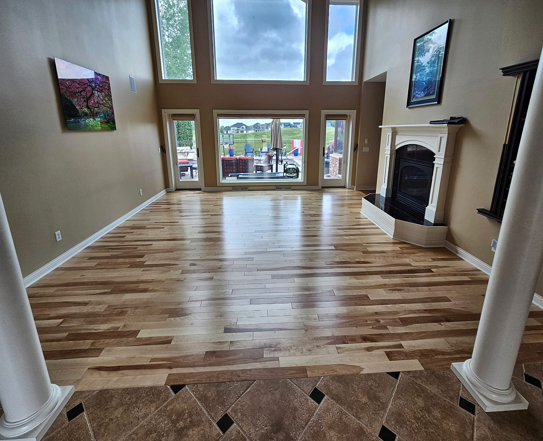 Natural hardwood flooring framed by a diagonal stone tile border in a two-story living room