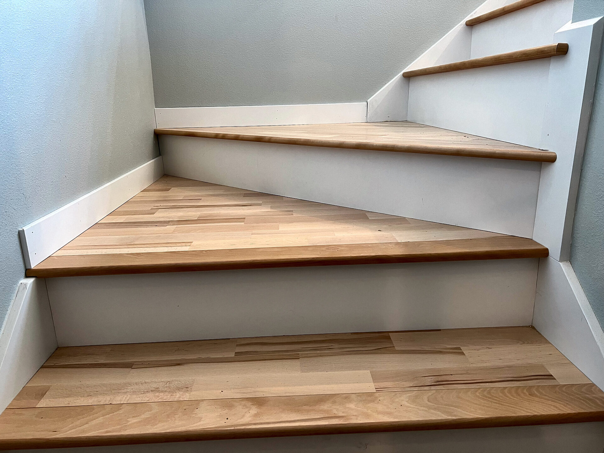 Hardwood stair treads turning through a winder section with white painted risers and skirt board
