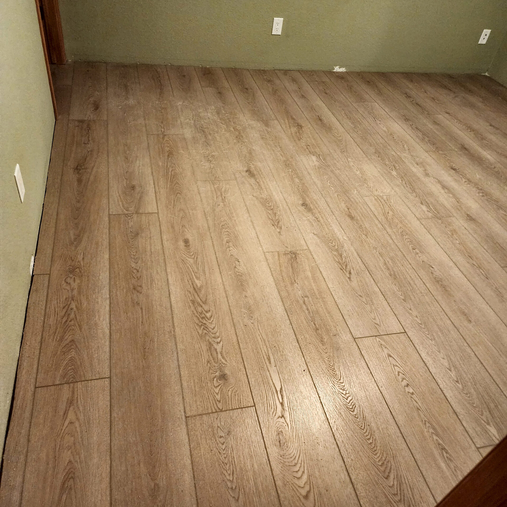 Wide light oak laminate planks installed across an empty room, ready for furniture