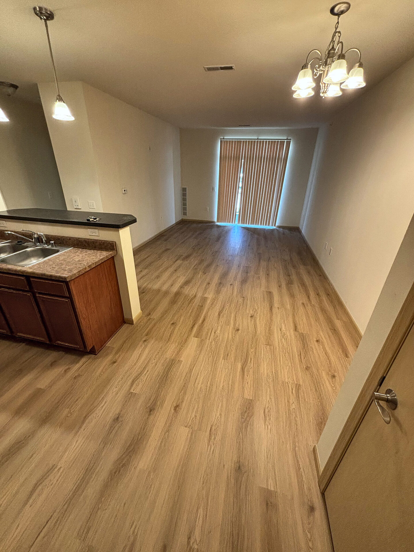 Warm oak vinyl plank flooring through an apartment kitchen and dining area toward a patio door