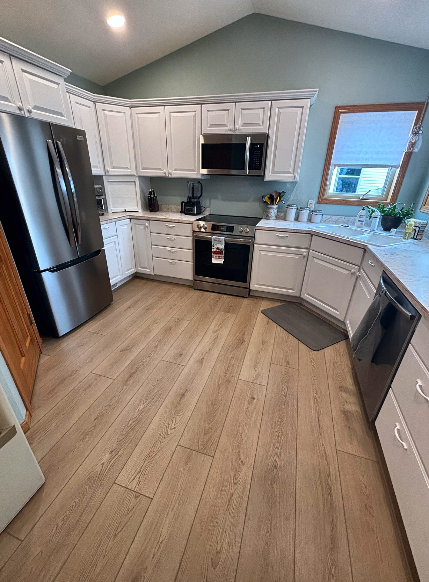 Light oak luxury vinyl plank flooring in a kitchen with white cabinets and stainless appliances