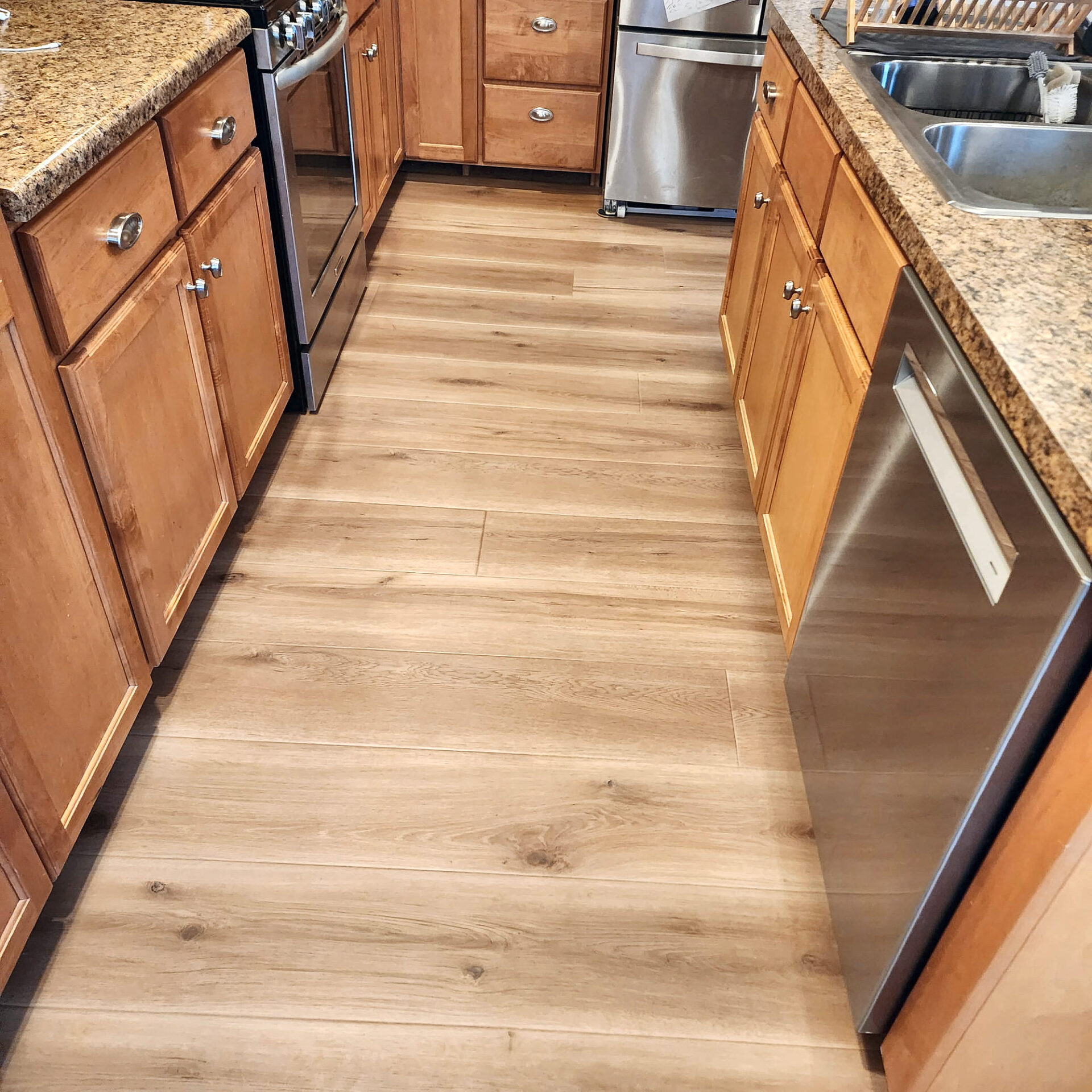 Light oak vinyl plank flooring running the length of a galley kitchen with maple cabinets