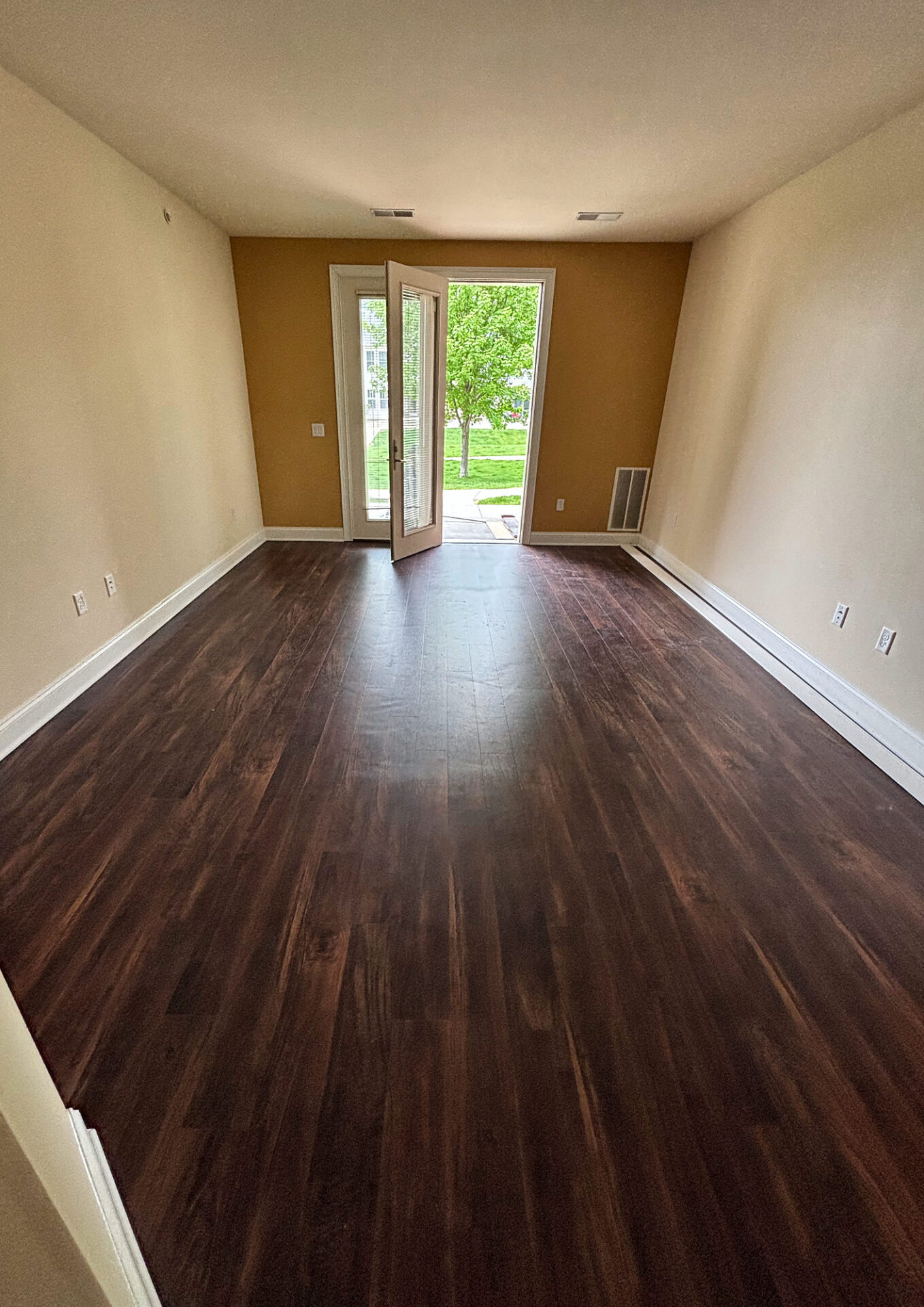 Dark wood-look vinyl plank flooring in a long empty living room leading to a patio door
