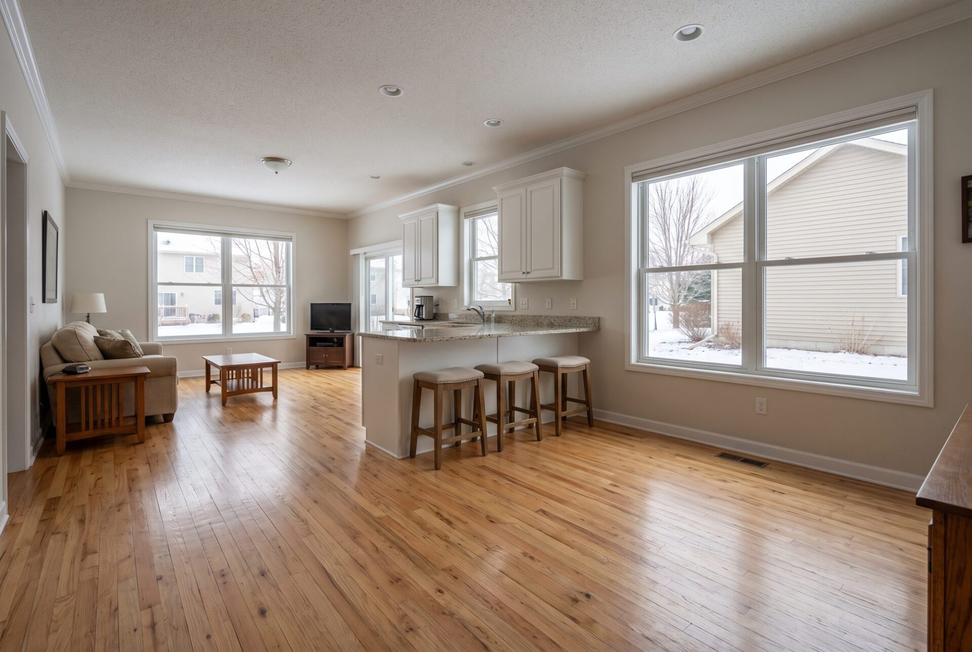 Natural red oak strip hardwood floor in a kitchen with white cabinets and a peninsula with stools