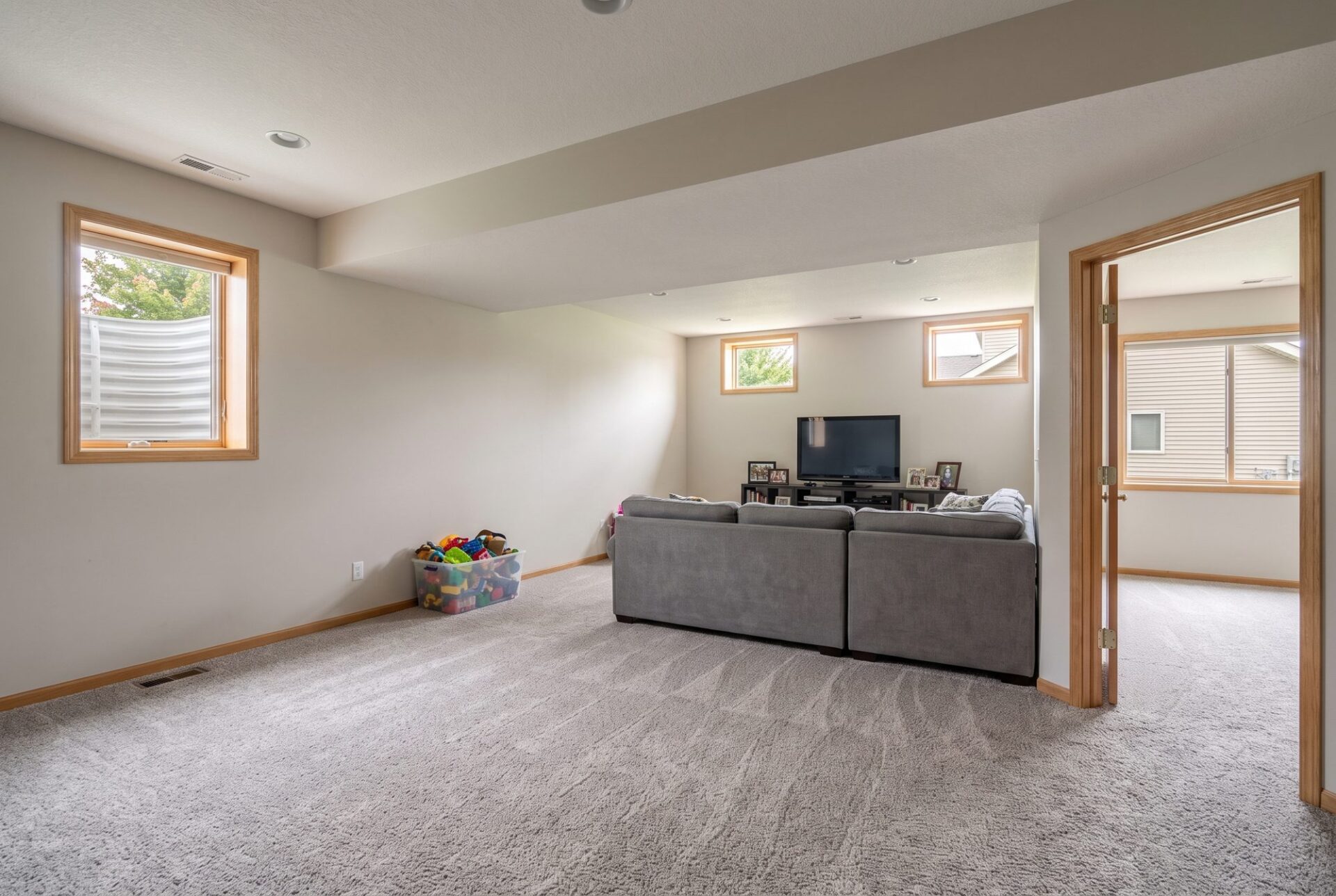 Soft gray-beige cut-pile carpet in a finished basement family room with a gray sectional and a toy bin