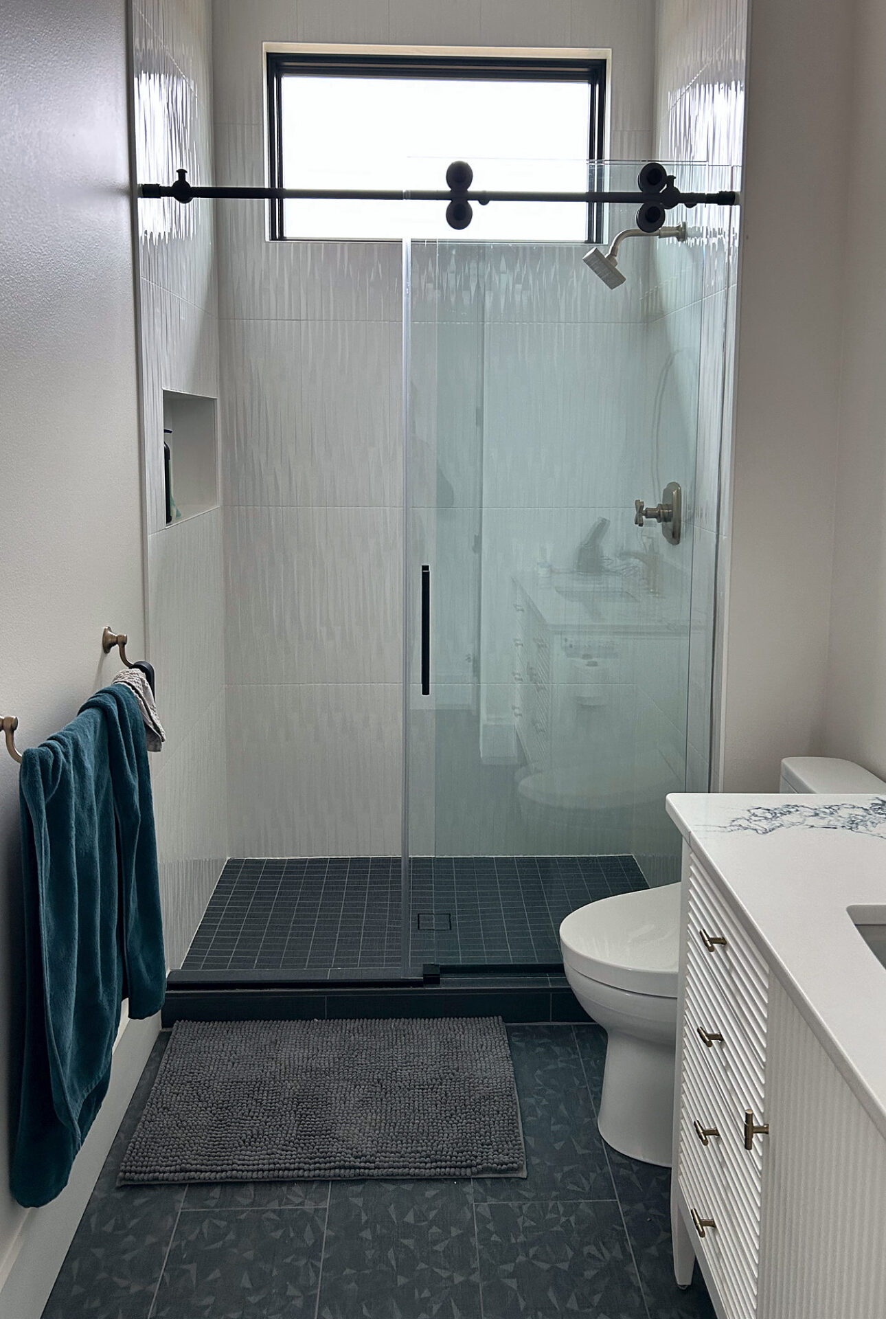 Charcoal patterned porcelain floor tile in a bathroom with a glass shower and white vanity