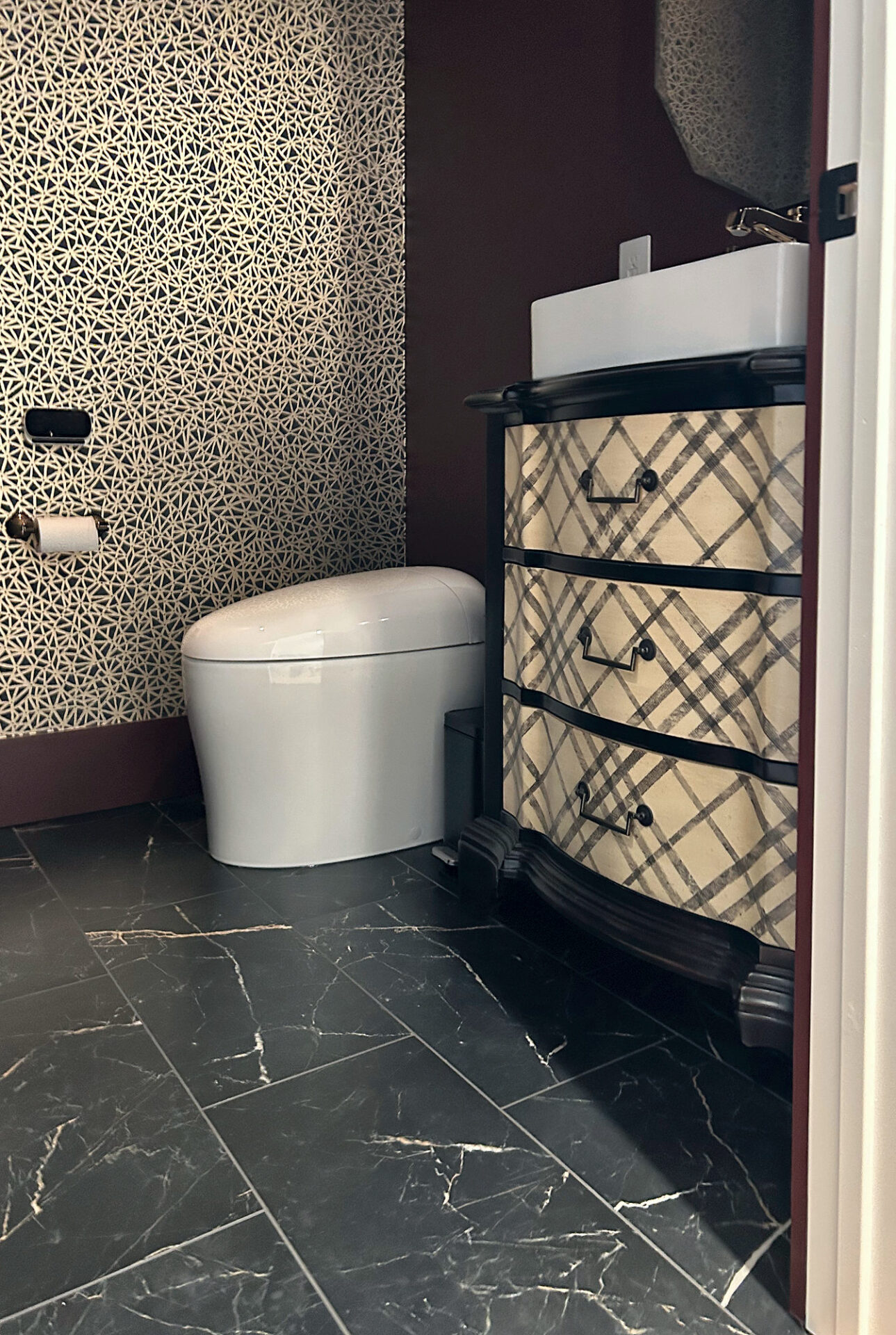Black marble-look porcelain tile with gold veining in a powder room with patterned wallpaper