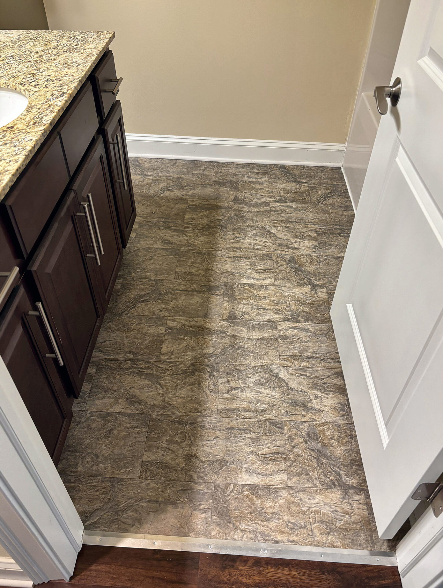 Stone-look luxury vinyl tile in a small bathroom beside a dark wood vanity