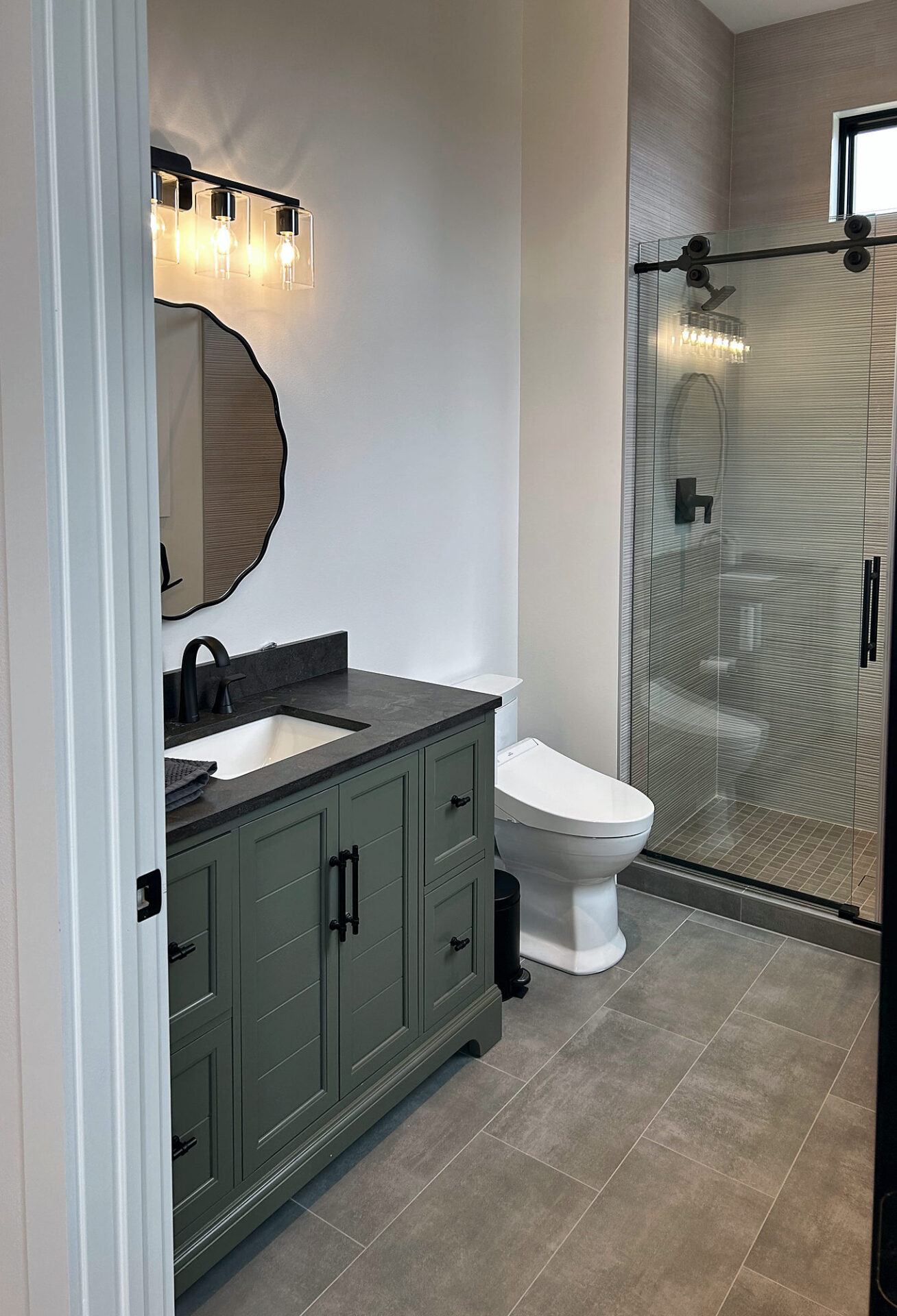 Gray large-format porcelain tile floor in a guest bathroom with green vanity and glass shower