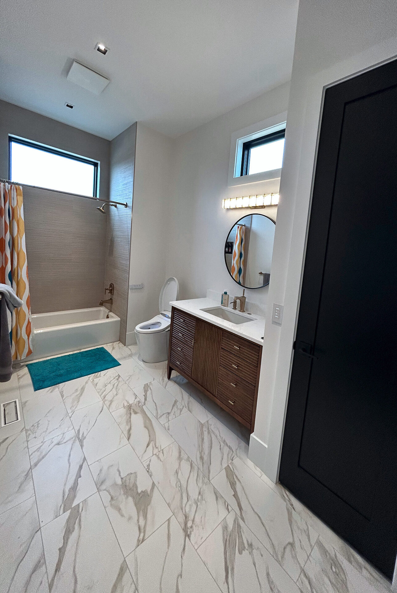 White marble-look porcelain tile floor in a hall bathroom with tub and wood vanity