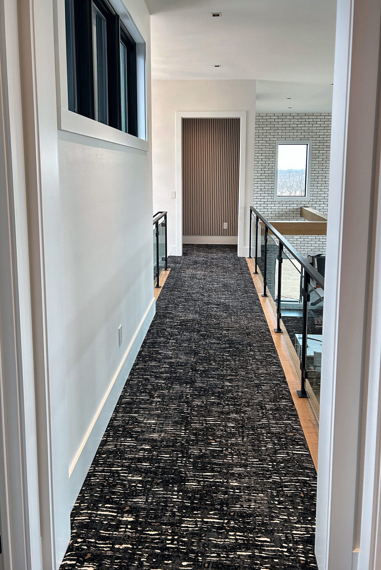 Patterned carpet runner along an upper hallway with oak edging and a glass railing