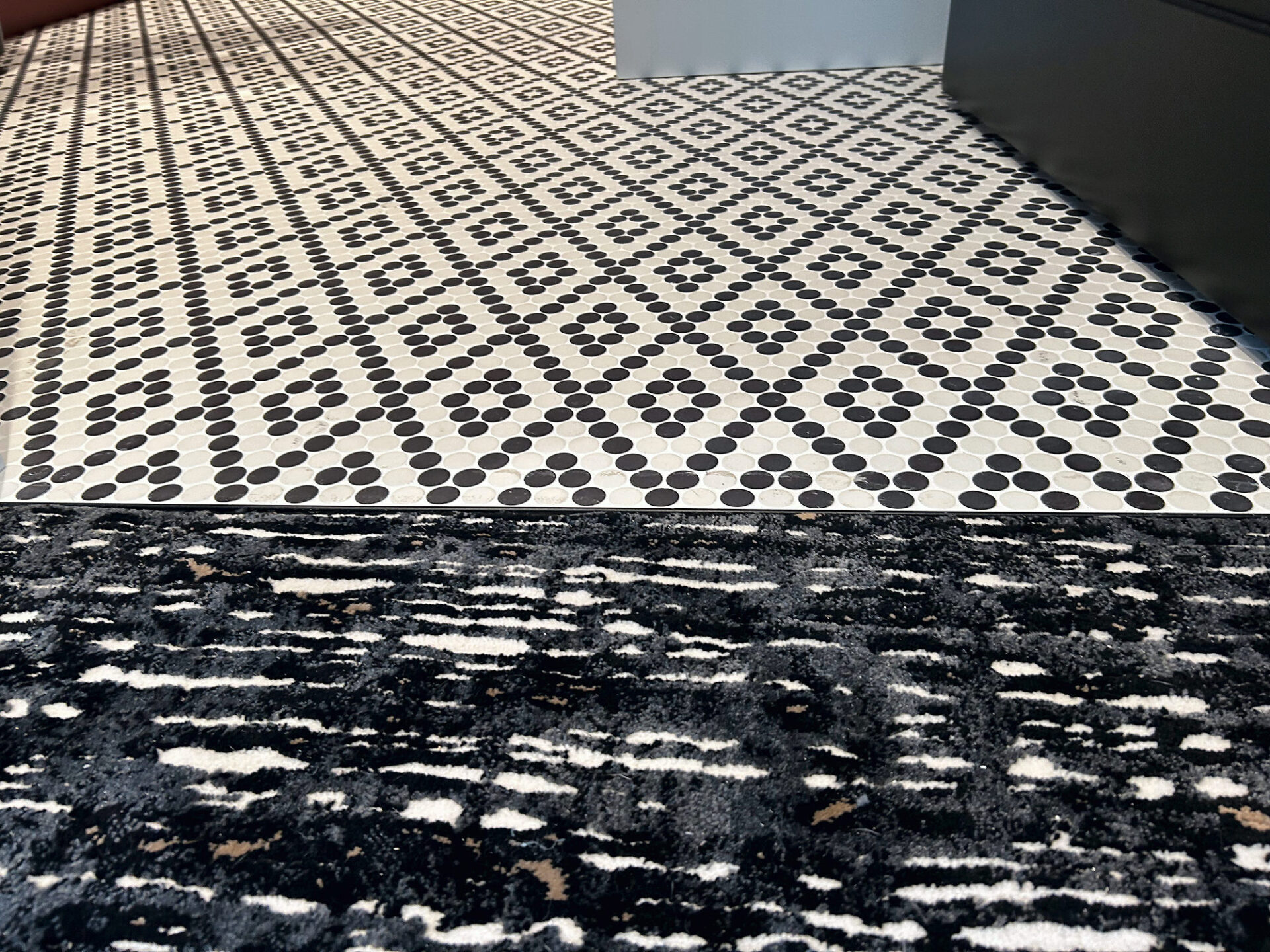 Black and white penny mosaic tile meeting a patterned carpet with a straight clean seam