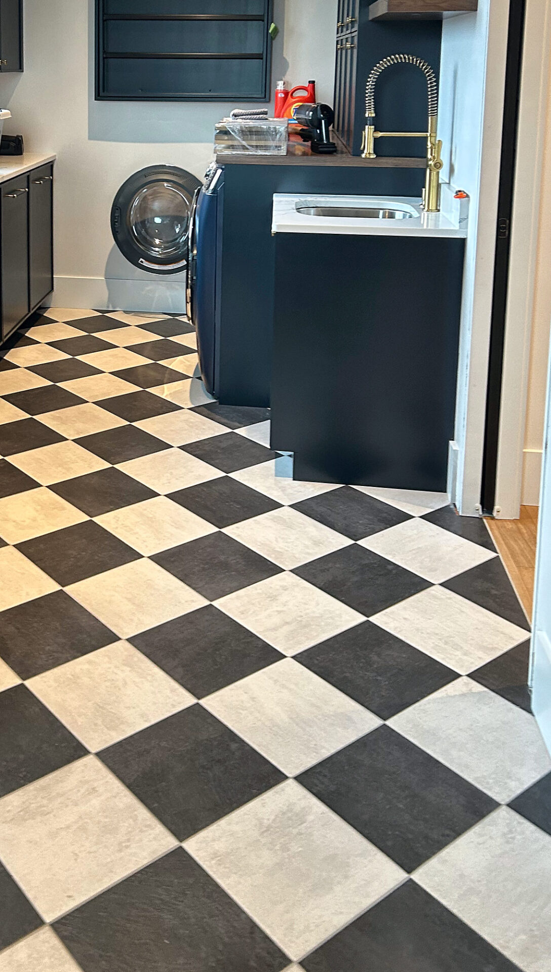 Black and white checkerboard tile floor in a mudroom with dark cabinets and a sink