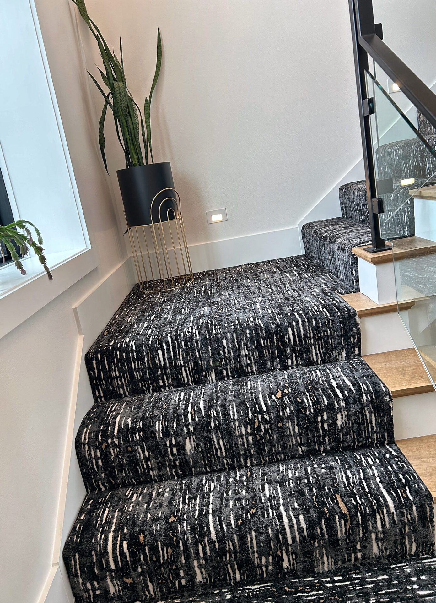Patterned carpet wrapped over stair nosings at a landing with oak treads and glass railing